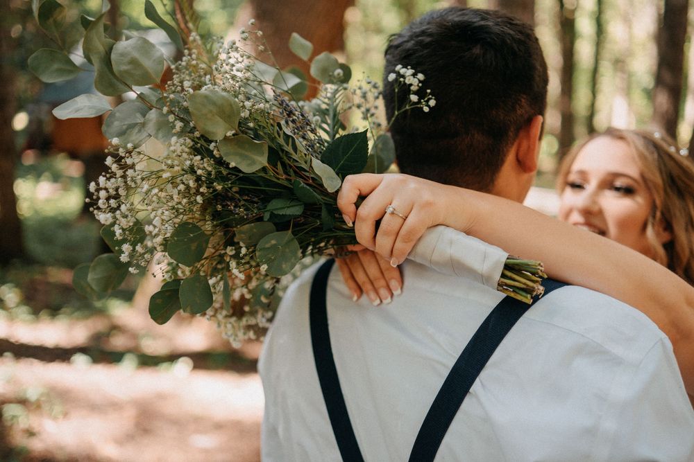 Wedding party embraces in a tender group hug moment during an outdoor forest celebration.