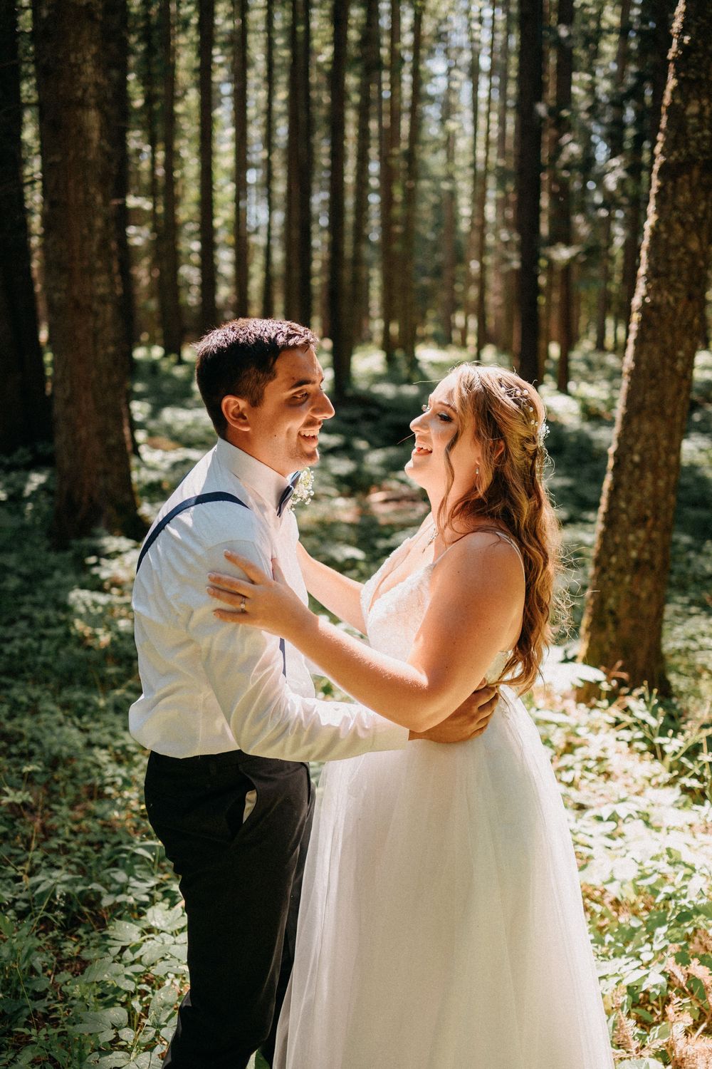 A couple shares a joyful dance together in a sunlit forest setting during their wedding celebration.