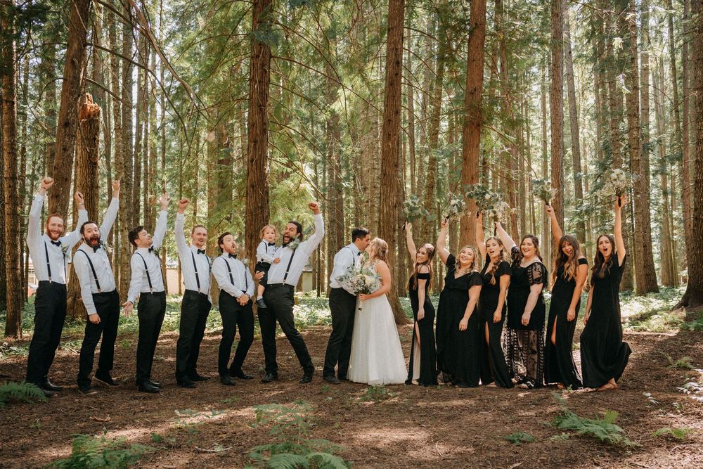 Wedding party stands in line among tall evergreen trees in a forest setting during a celebration.