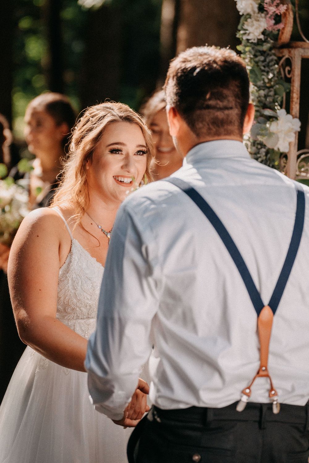 A wedding ceremony moment in a forest setting with sunlight filtering through the trees.