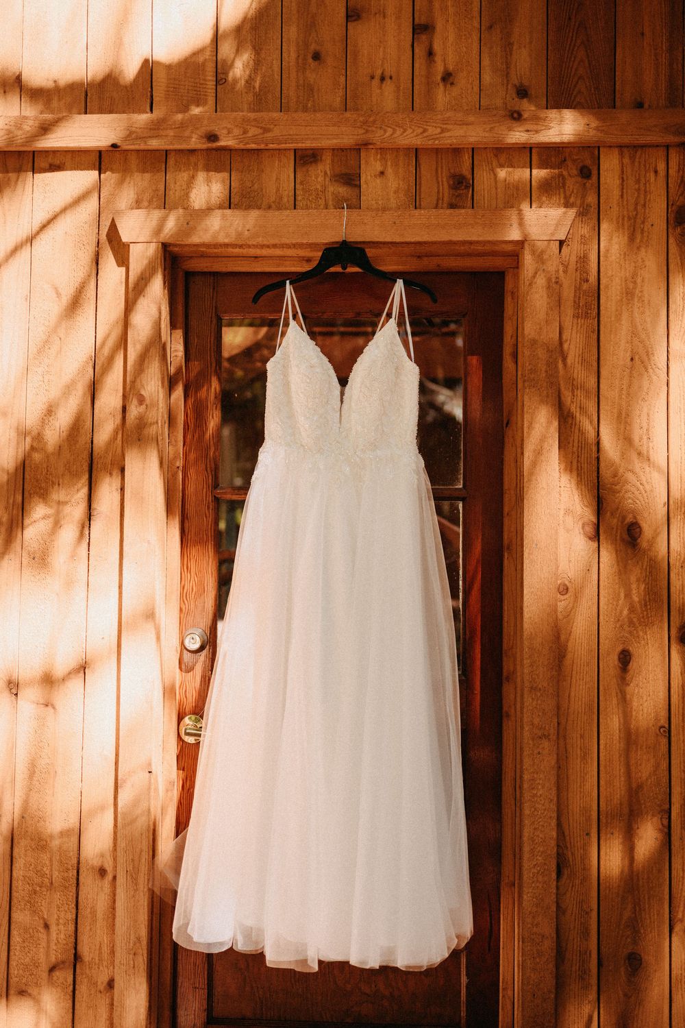 White wedding dresses hanging on wooden wall in rustic barn setting with natural lighting.