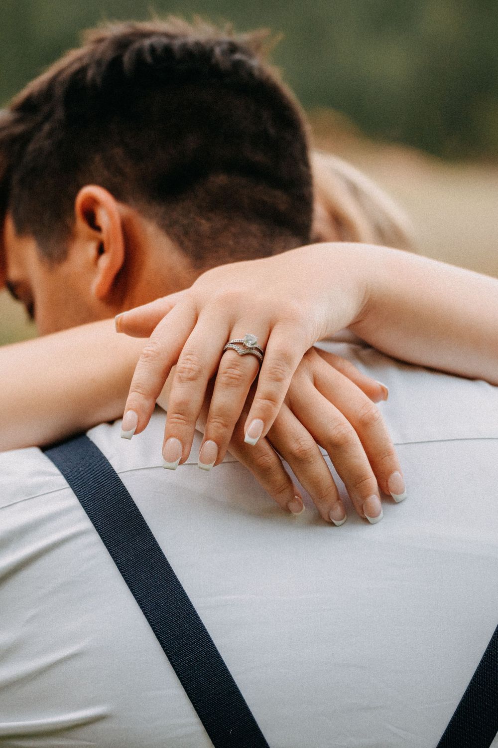 Detail shot of hands resting on shoulders showing wedding rings and formal attire.