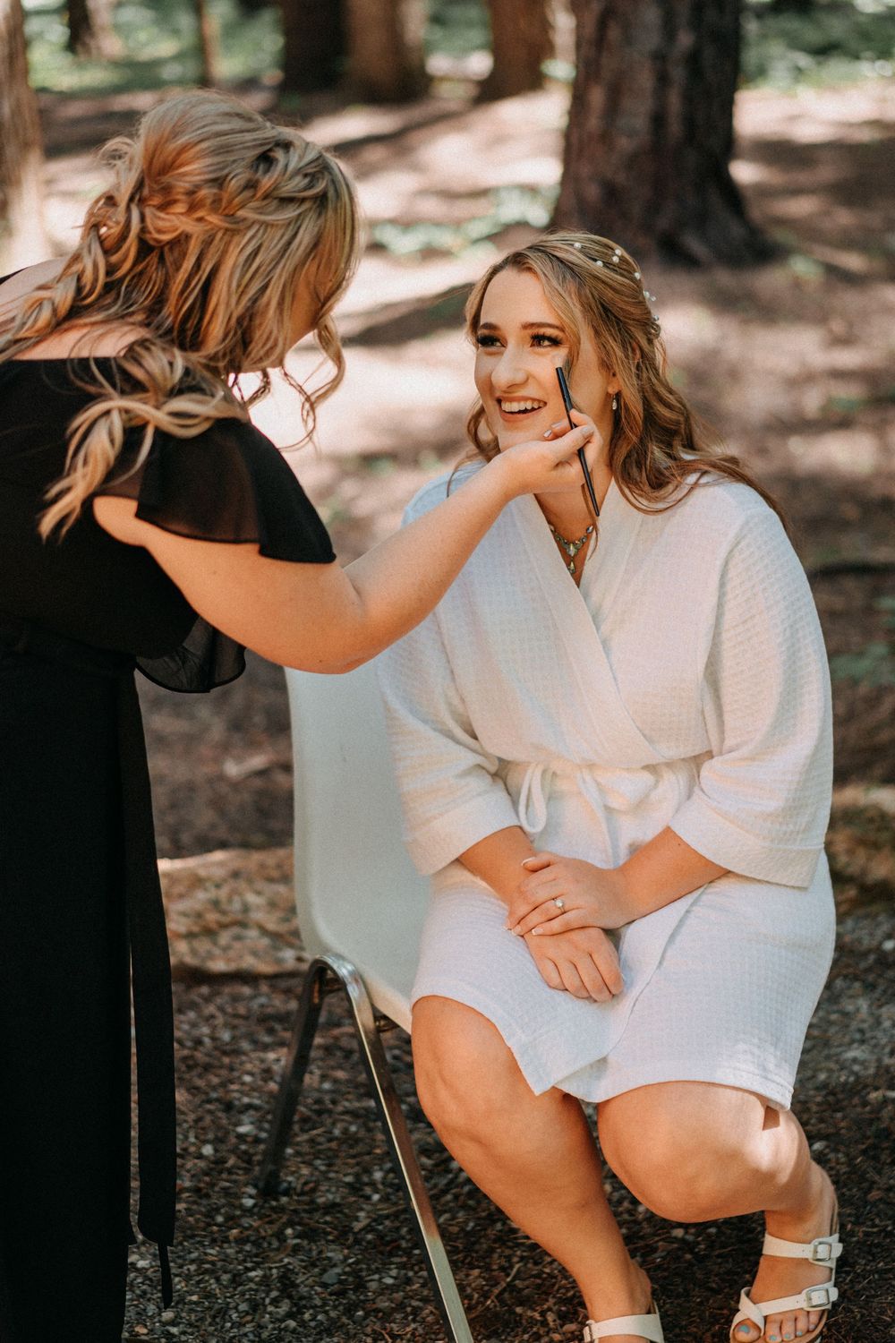 Wedding preparation moment in white robe seated outdoors in forest setting.