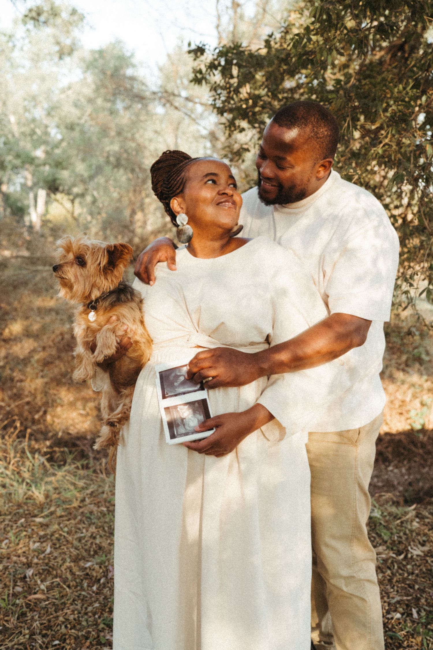 Couple poses with their dog and ultrasound photo during outdoor maternity session.