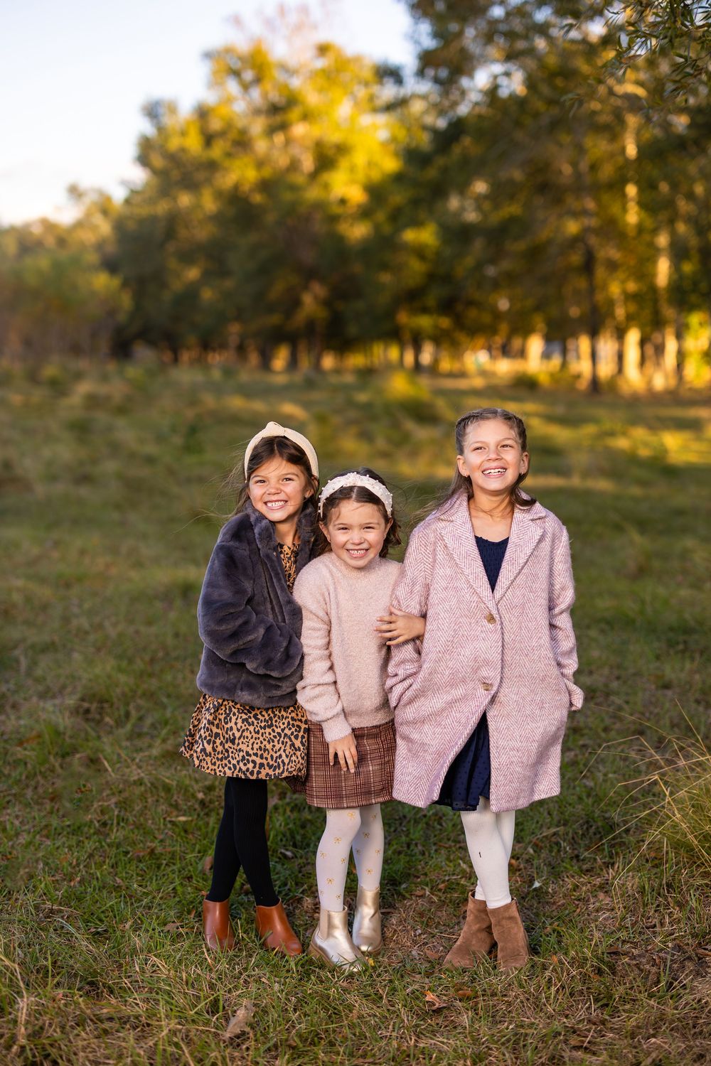 Three small children in coordinating outfits laughing together outdoors at sunset.