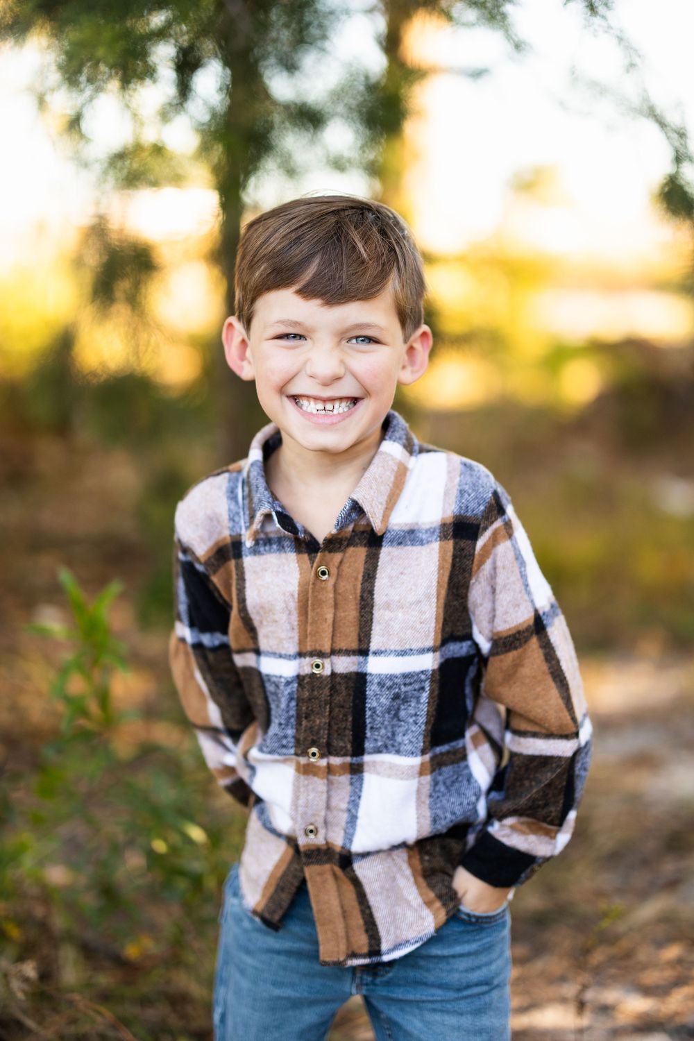 Young boy in plaid shirt smiles brightly in outdoor autumn setting.