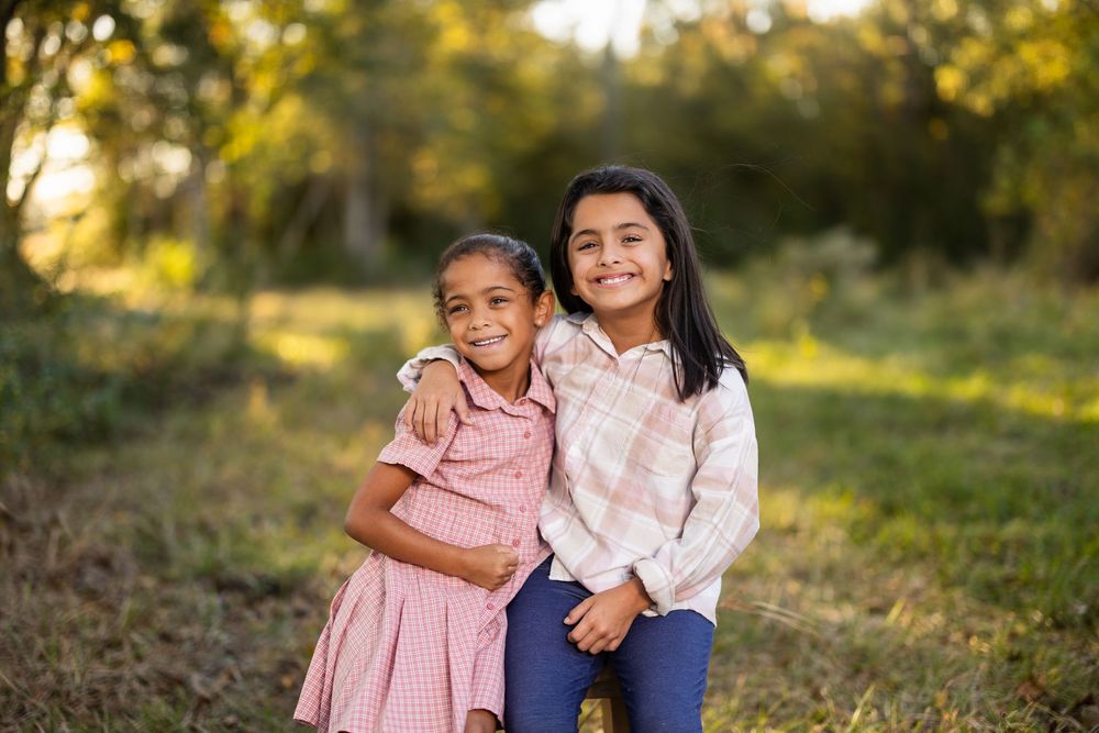 Two children sit close together outdoors during golden hour.