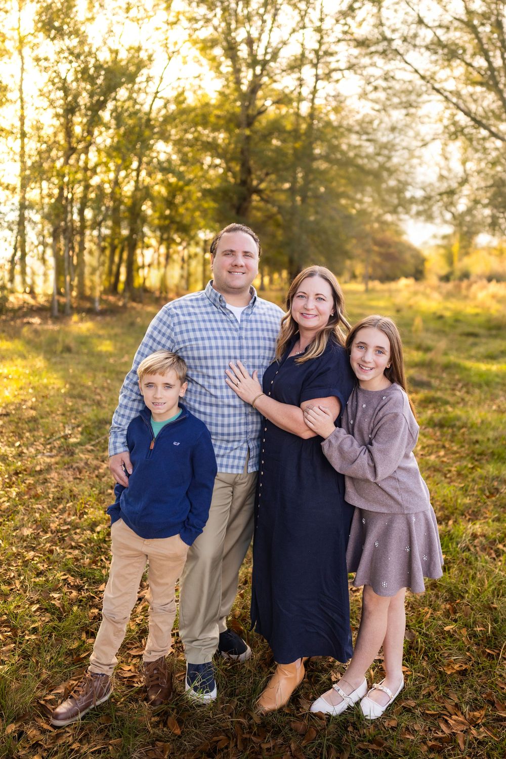 A family of four poses together in a wooded setting during sunset.