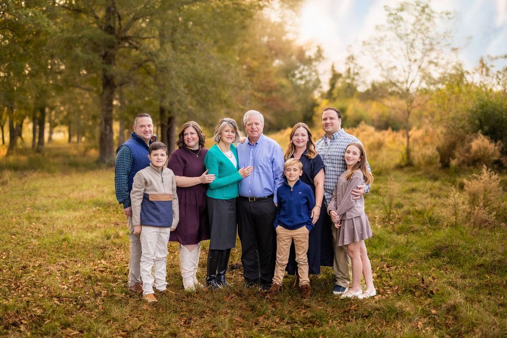 A large family group poses together outdoors during golden hour in autumn.