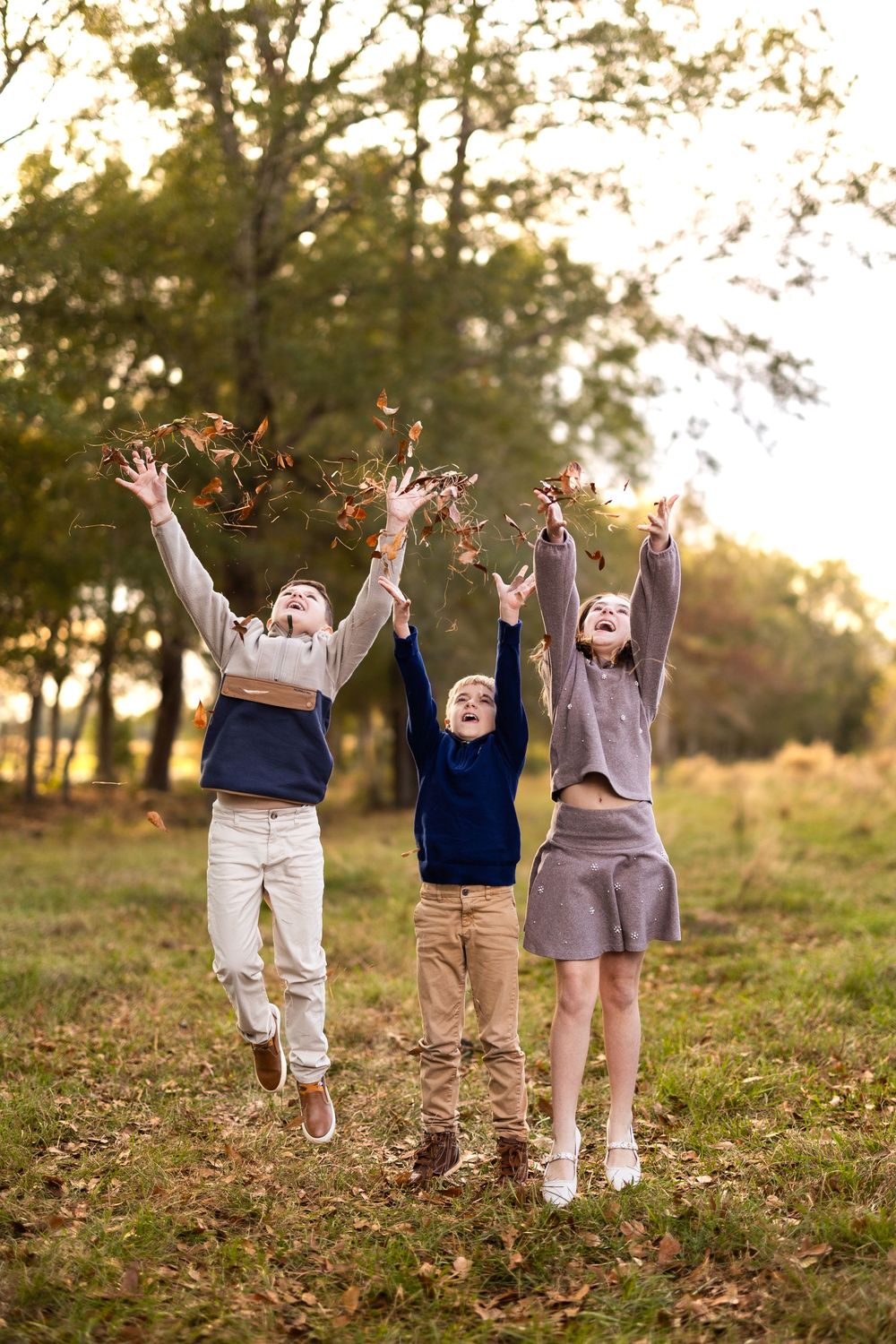 Three people joyfully throw autumn leaves in the air during a fall photoshoot.