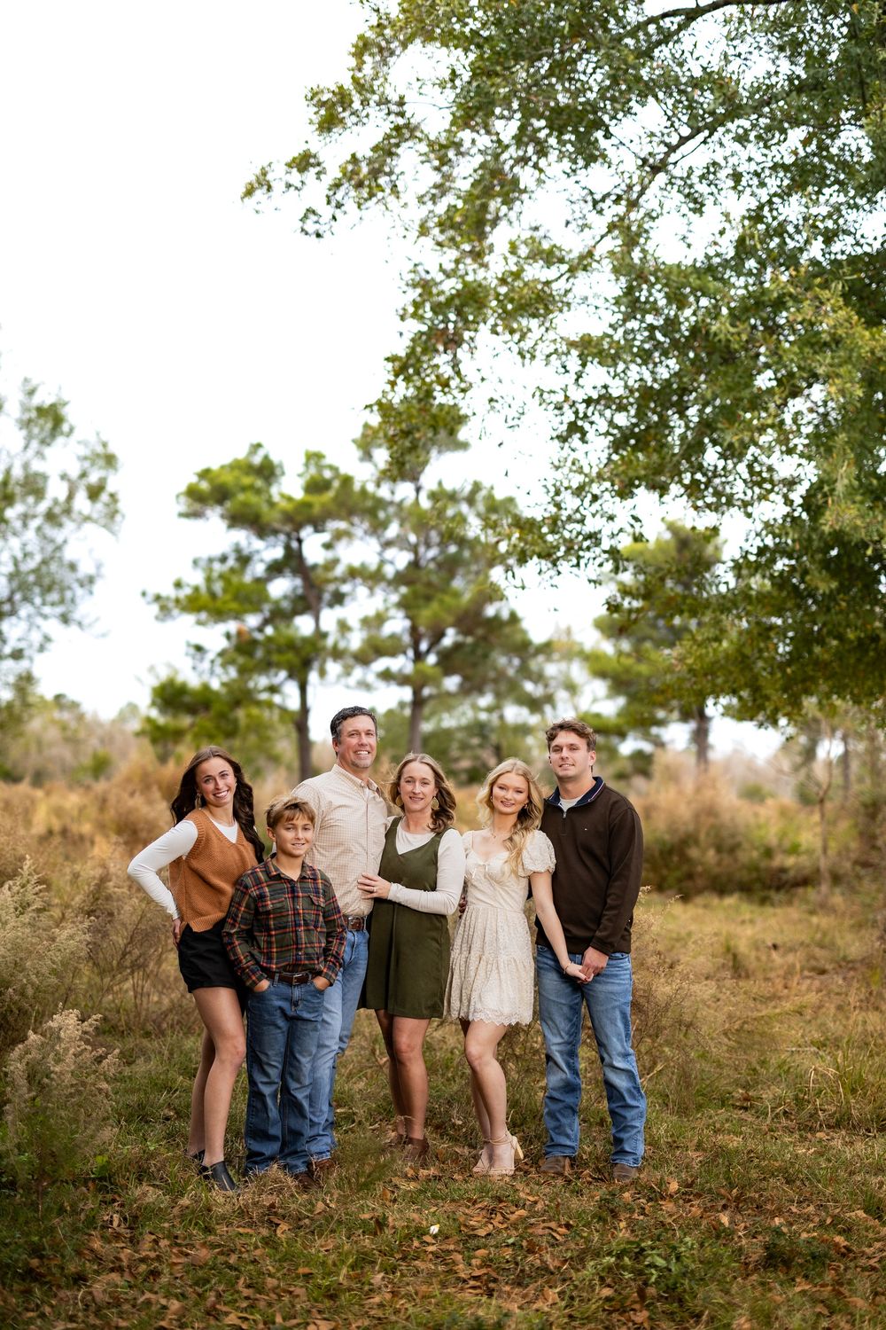 A casual outdoor family portrait in a natural setting with tall pine trees and golden grass.