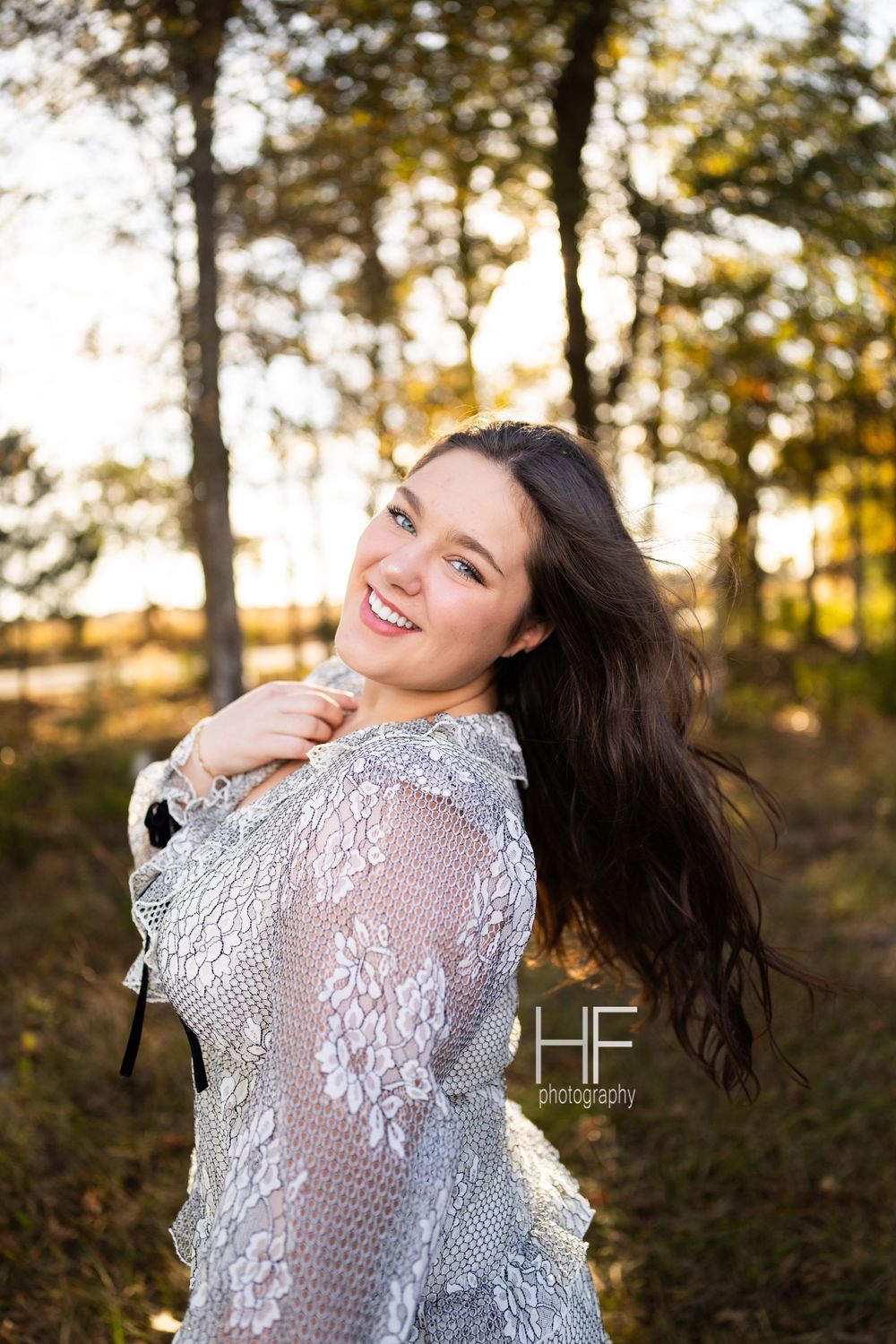 Joyful portrait in lace dress with windswept hair against autumn trees.