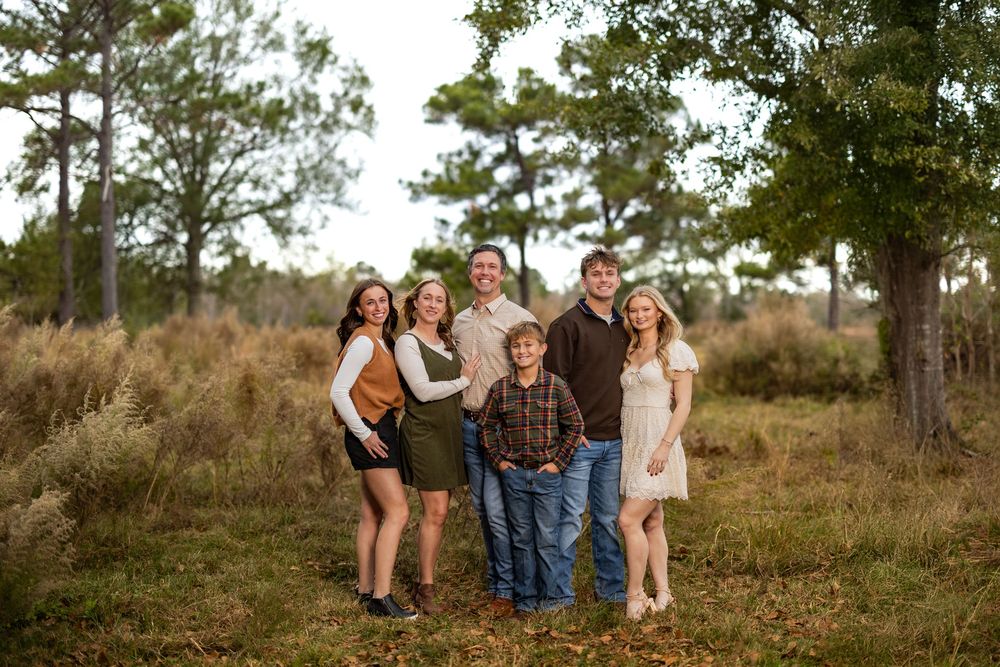 Family members gather for a portrait in a rustic outdoor setting with pine trees.