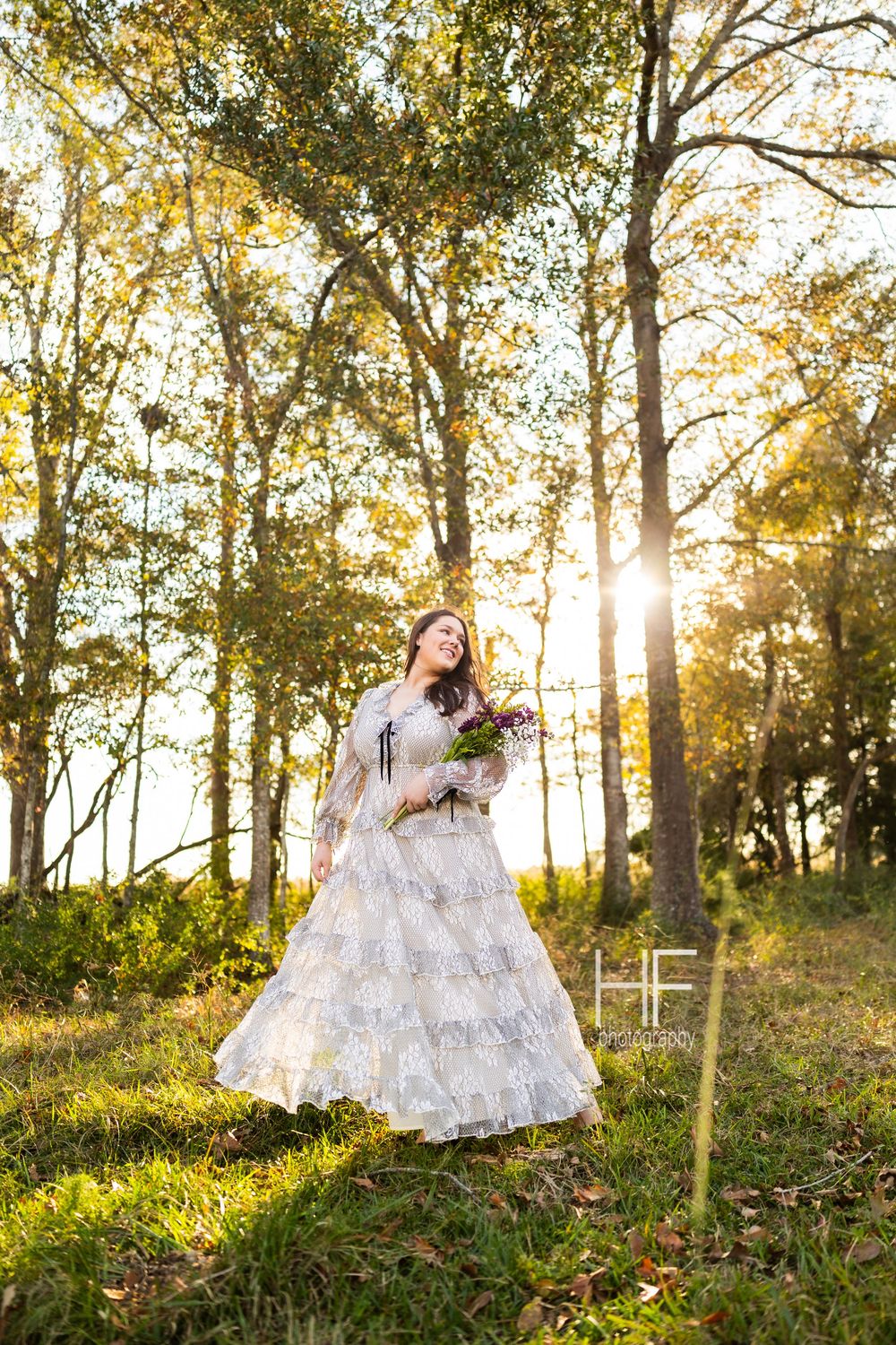 Person in flowing white lace dress twirling in sunlit autumn forest setting.