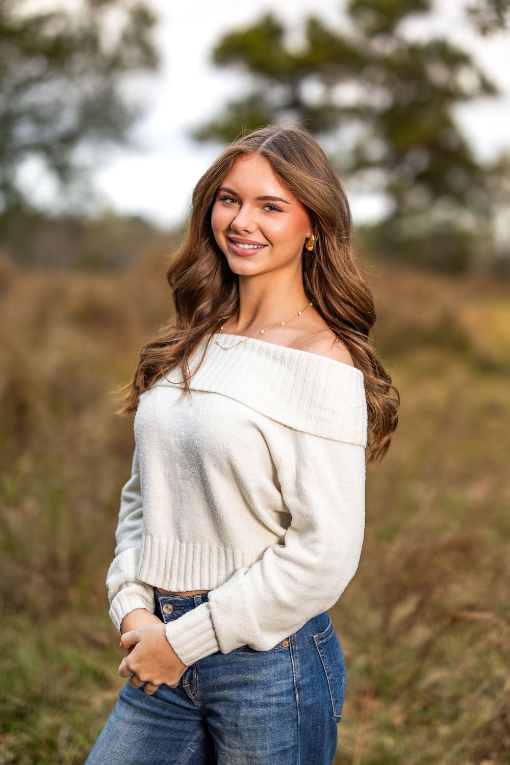 Portrait of person in cream sweater and jeans against natural outdoor backdrop.