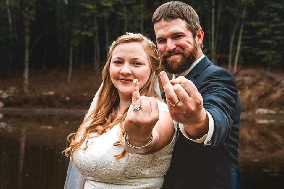 Wedding portrait by Northern Exposure featuring a bride and groom holding up their ring fingers for the camera.