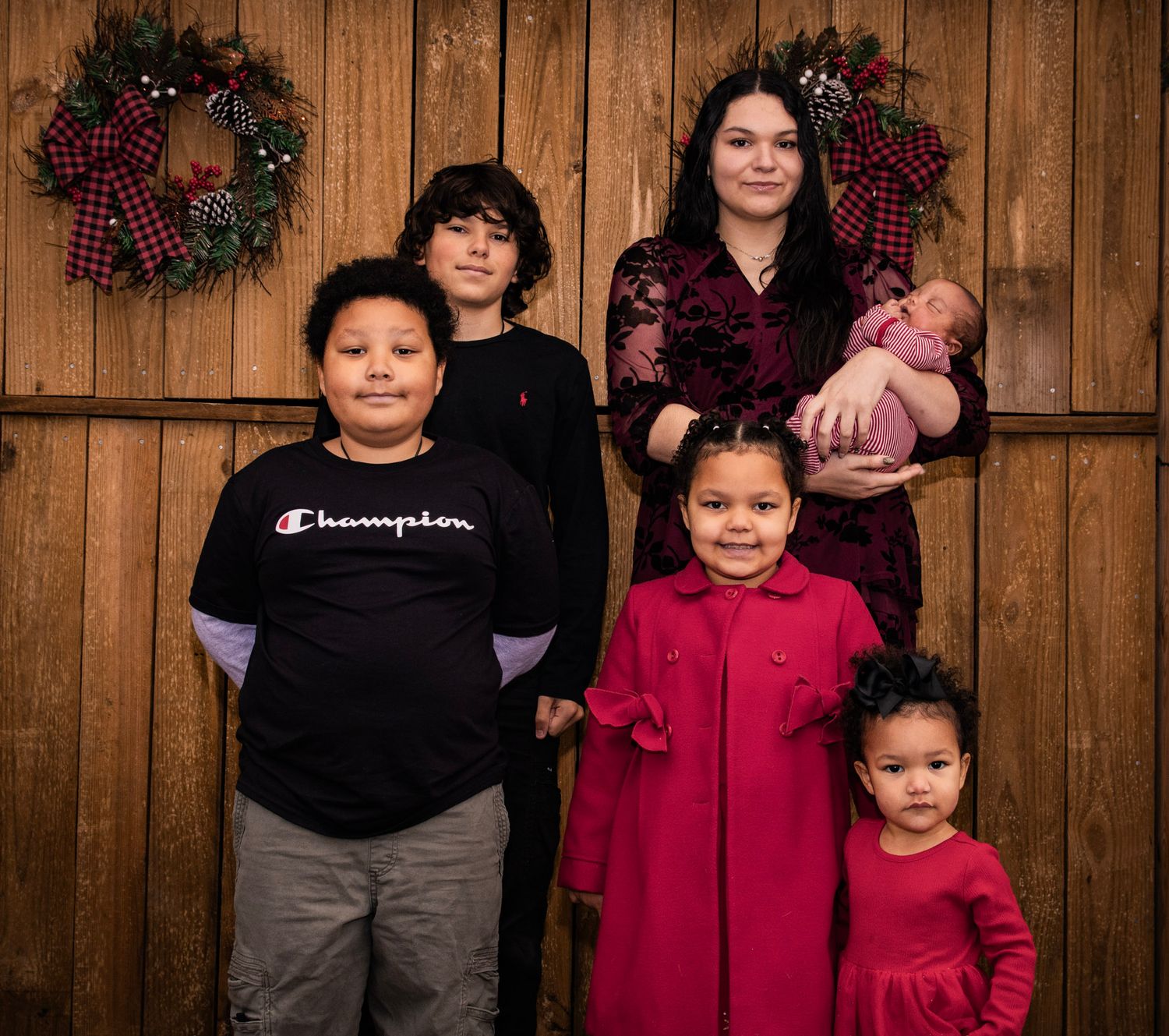 A group poses against a wooden wall decorated with holiday wreaths and plaid bows.