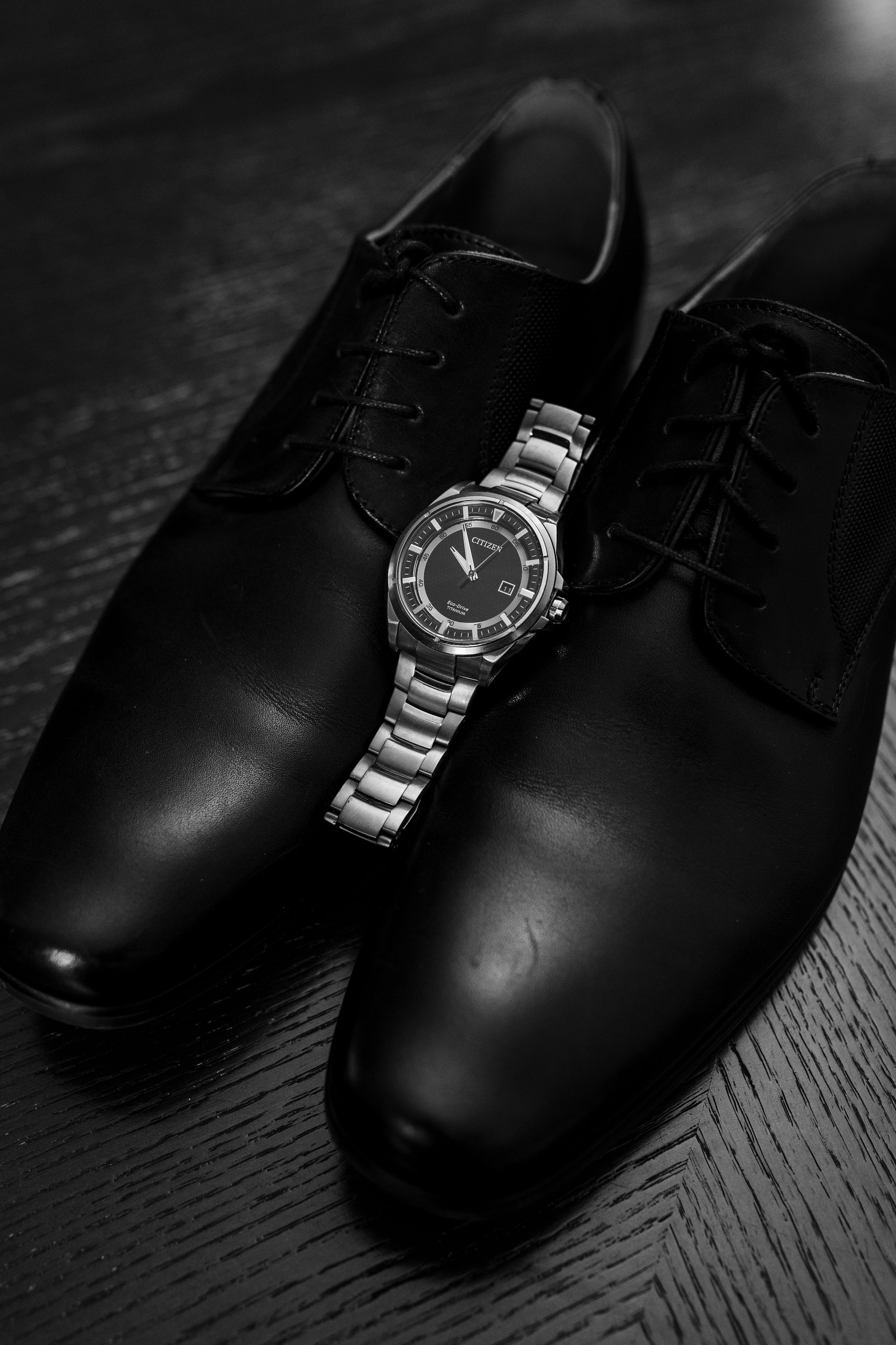 Black leather dress shoes arranged in a row with varying lighting and angles on a dark wooden surface.