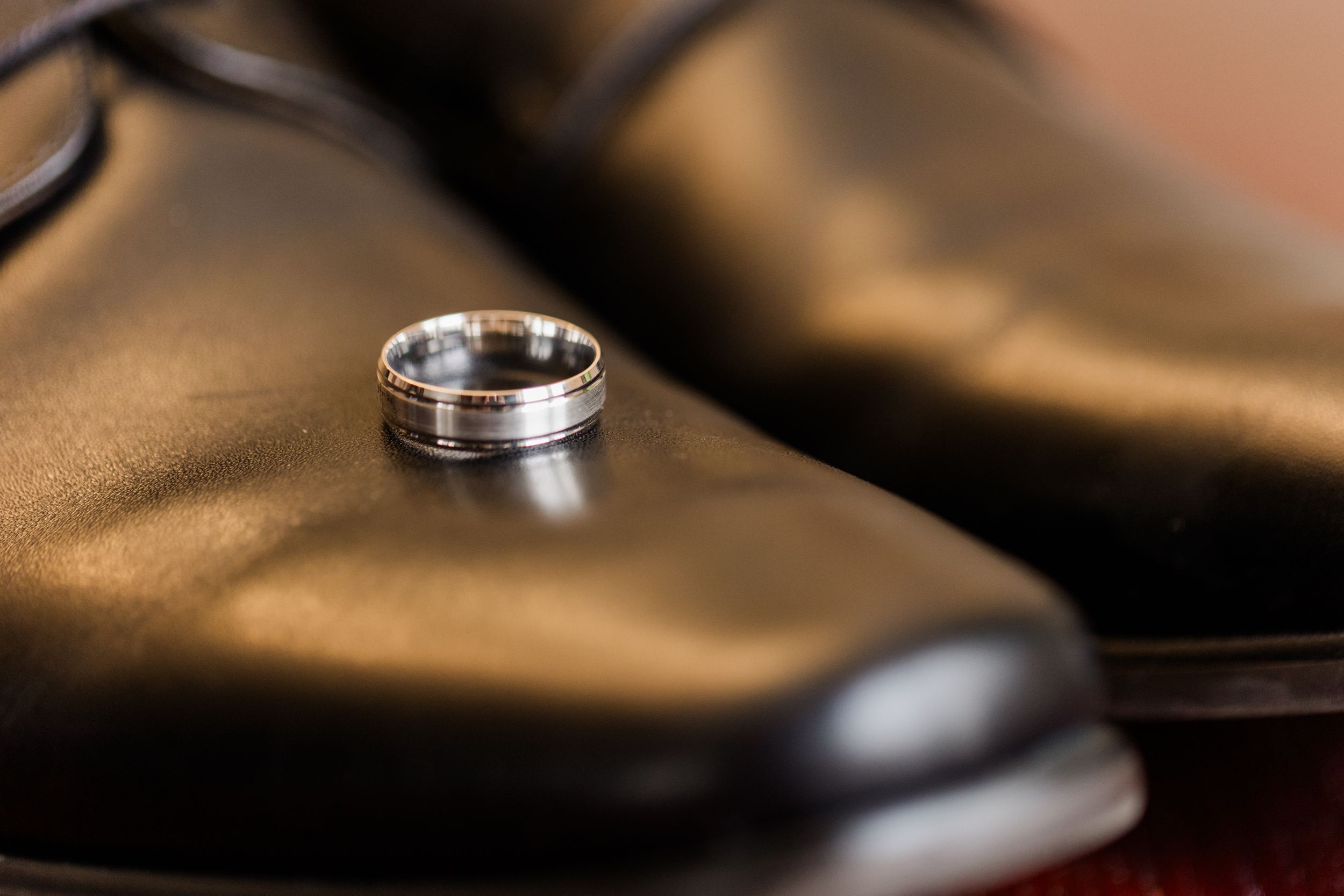 Close-up macro shot of a silver wedding ring with textured details on a brown leather surface.