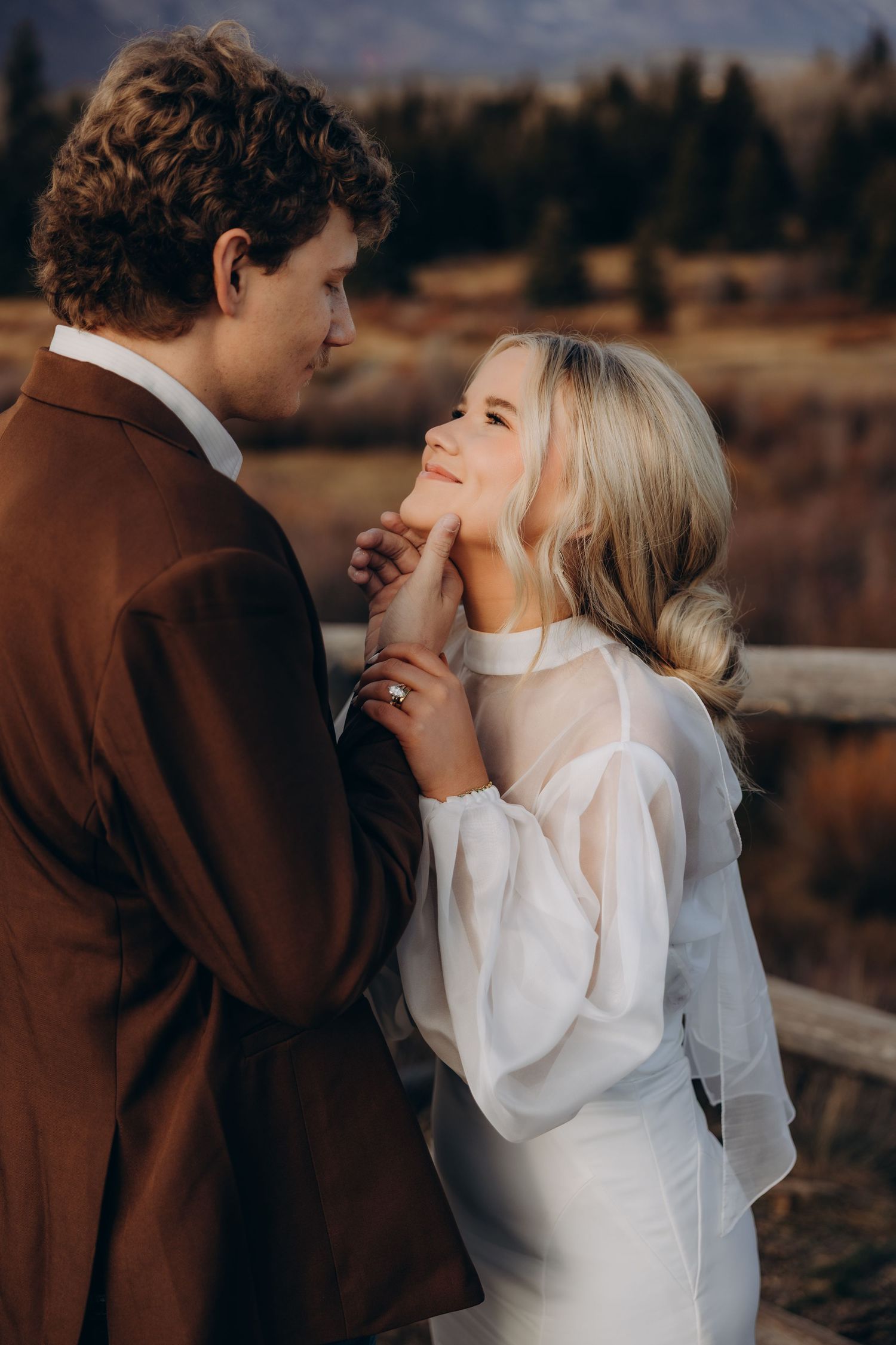 Romantic moment captured between a couple in white and brown attire during a countryside photoshoot.