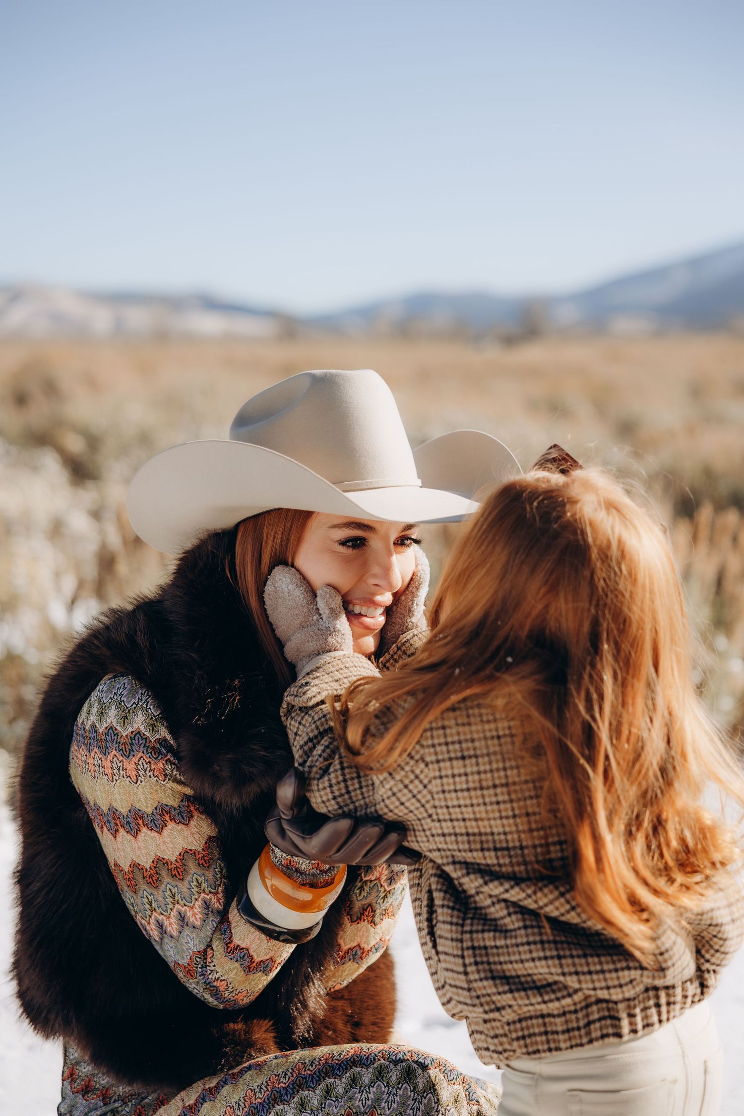 A romantic couple in western attire embracing in a desert landscape during sunset.