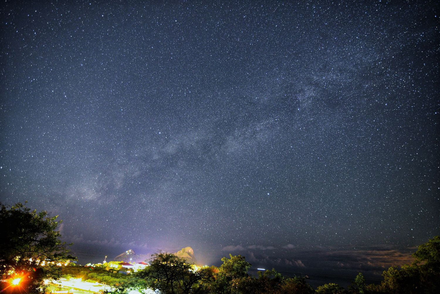 Stunning panoramic view of starry night sky with distant city lights on horizon.