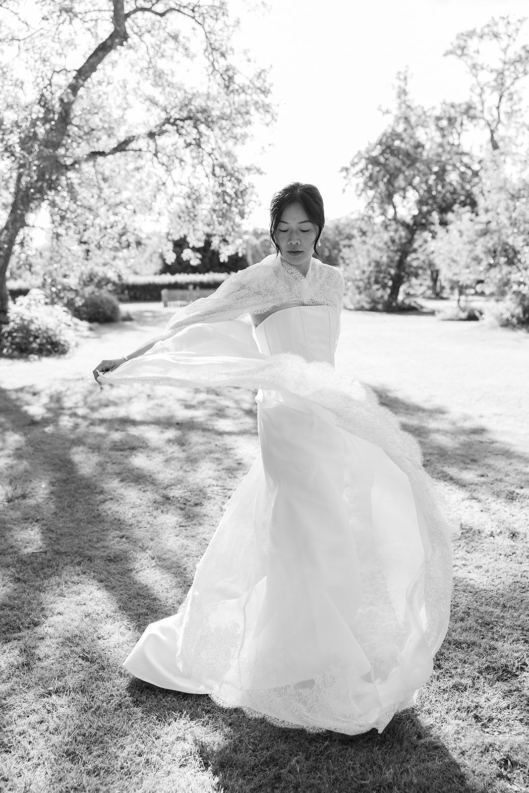 A flowing white dress twirls gracefully in a sunlit garden setting with trees in the background.