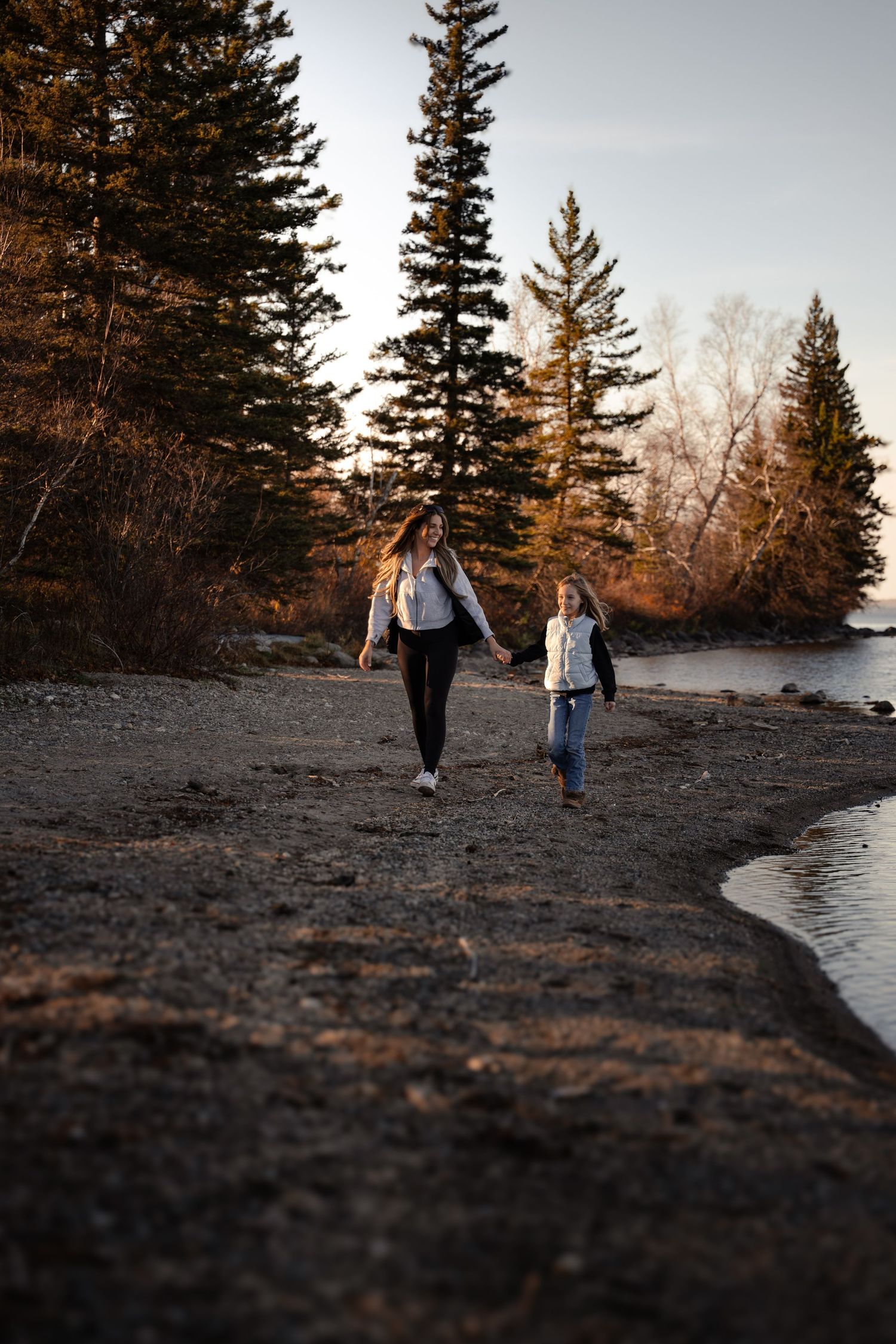 Scenic lakeside path with evergreen trees at sunset.