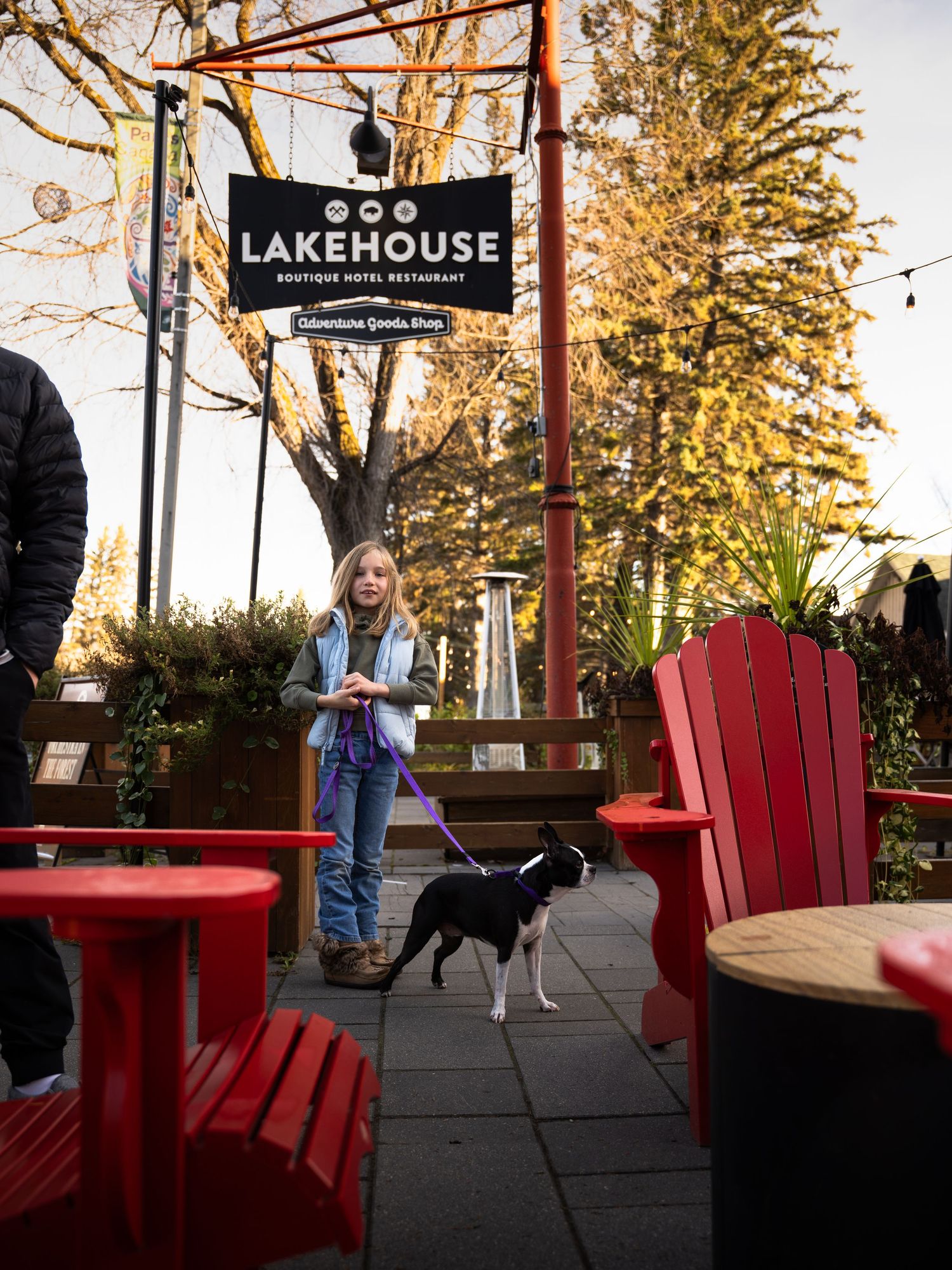 Black and white dog stands on patio deck under Lakehouse restaurant sign with red Adirondack chairs.