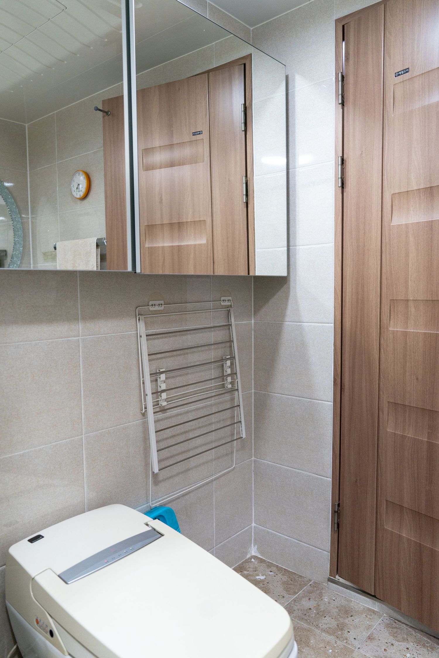Modern bathroom interior with wooden doors, wall-mounted towel rack, and white toilet in neutral tiled space.