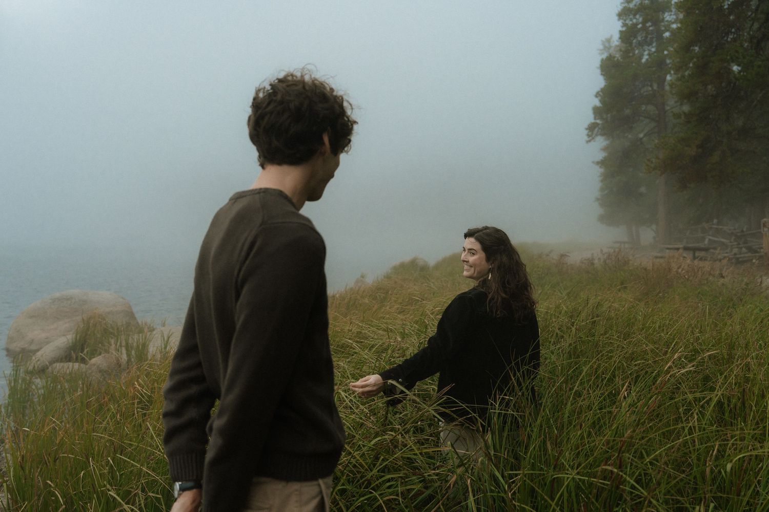 Romantic couple lying in tall grass field wearing white and earth-toned clothing.