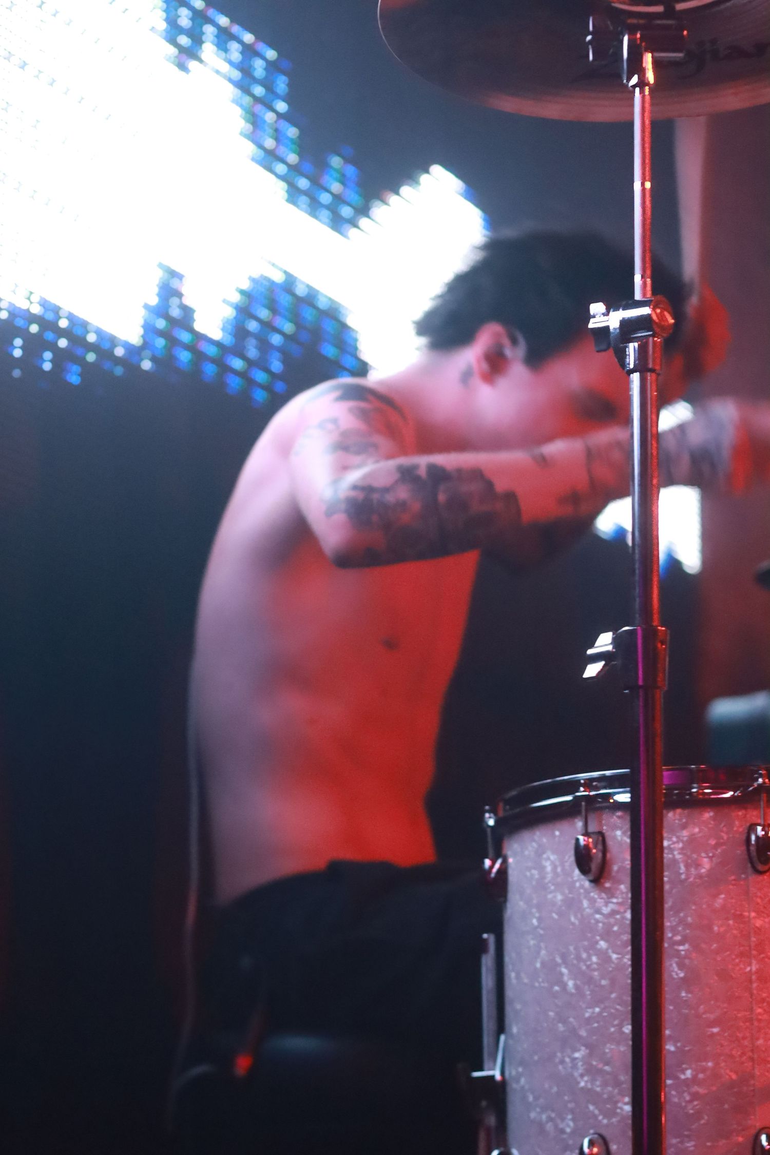 Drummer performing on stage with sparkling drum kit under blue lighting effects during live concert performance.