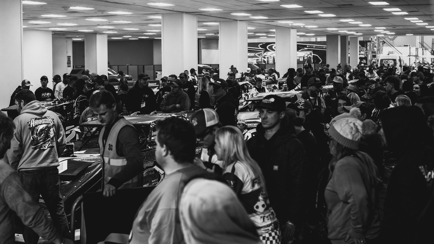 Long queue of people waiting in line at an indoor shopping mall or transit station with illuminated signs.