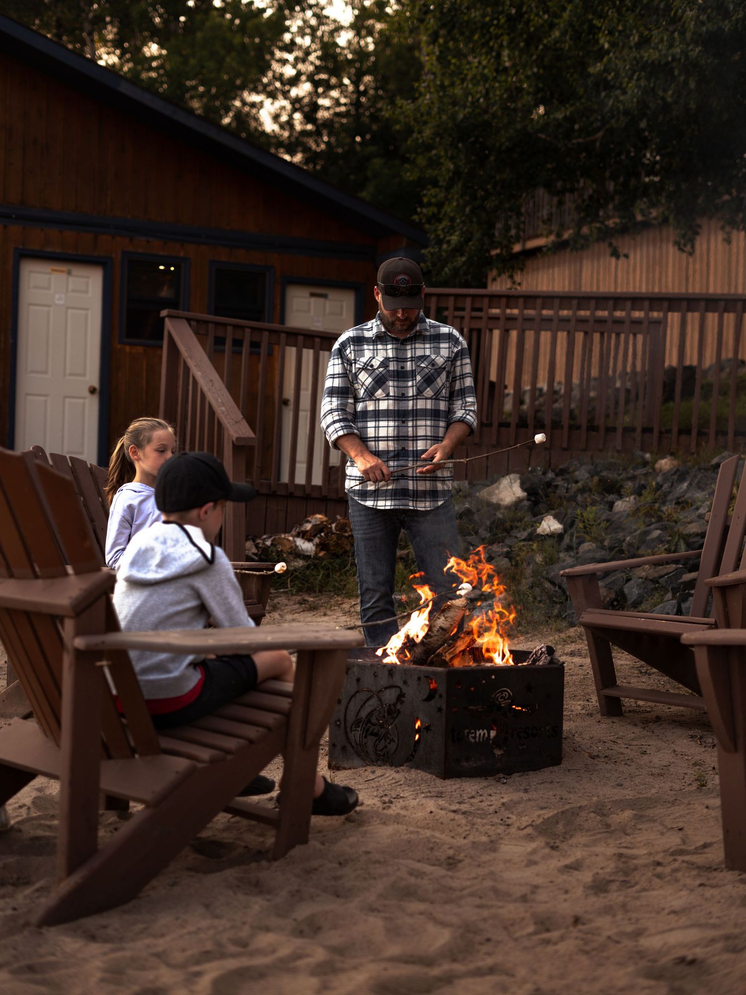 People gathered around a campfire in Adirondack chairs at dusk.