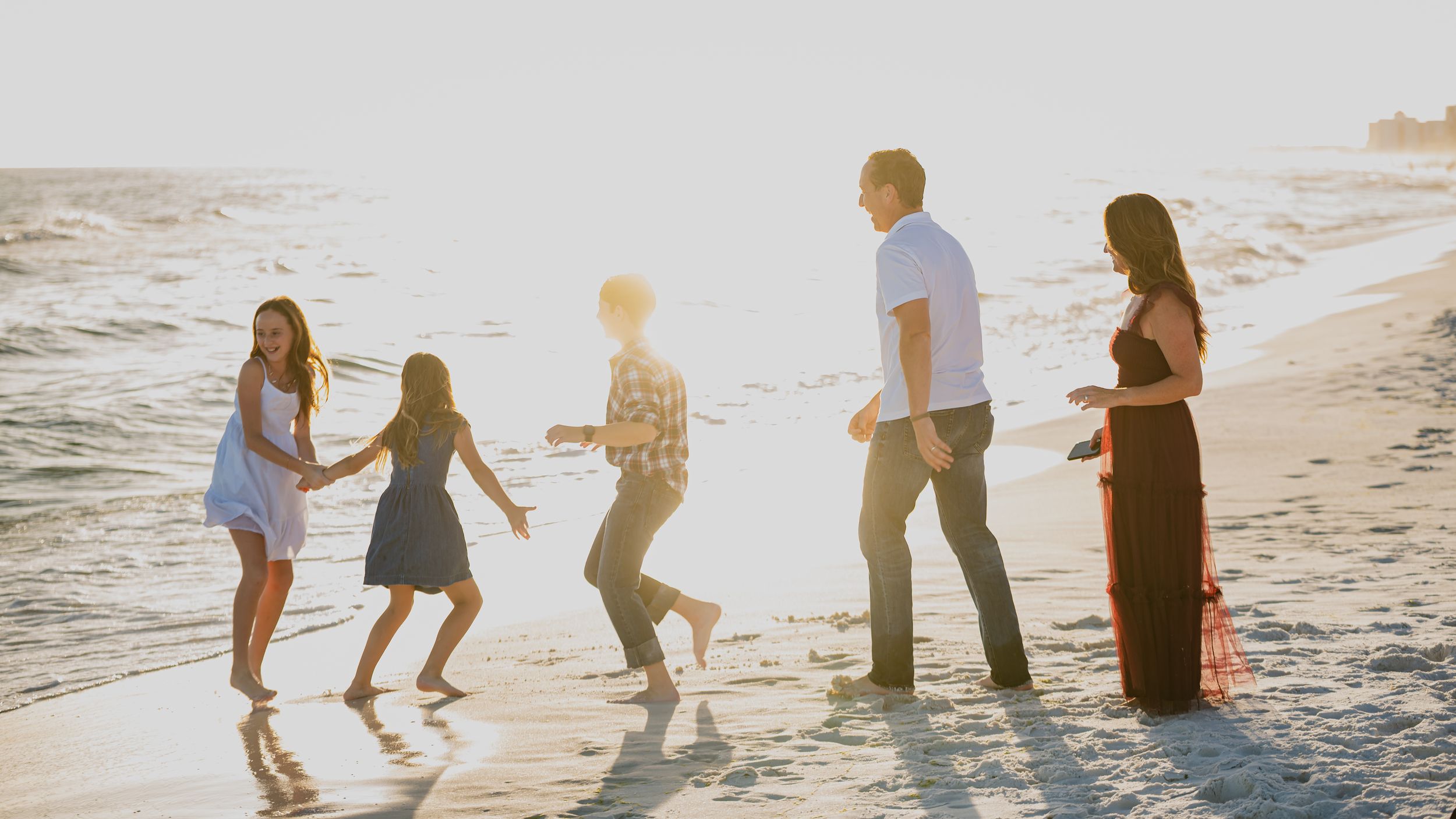 Silhouettes of a family playing and walking along the shoreline at sunset.