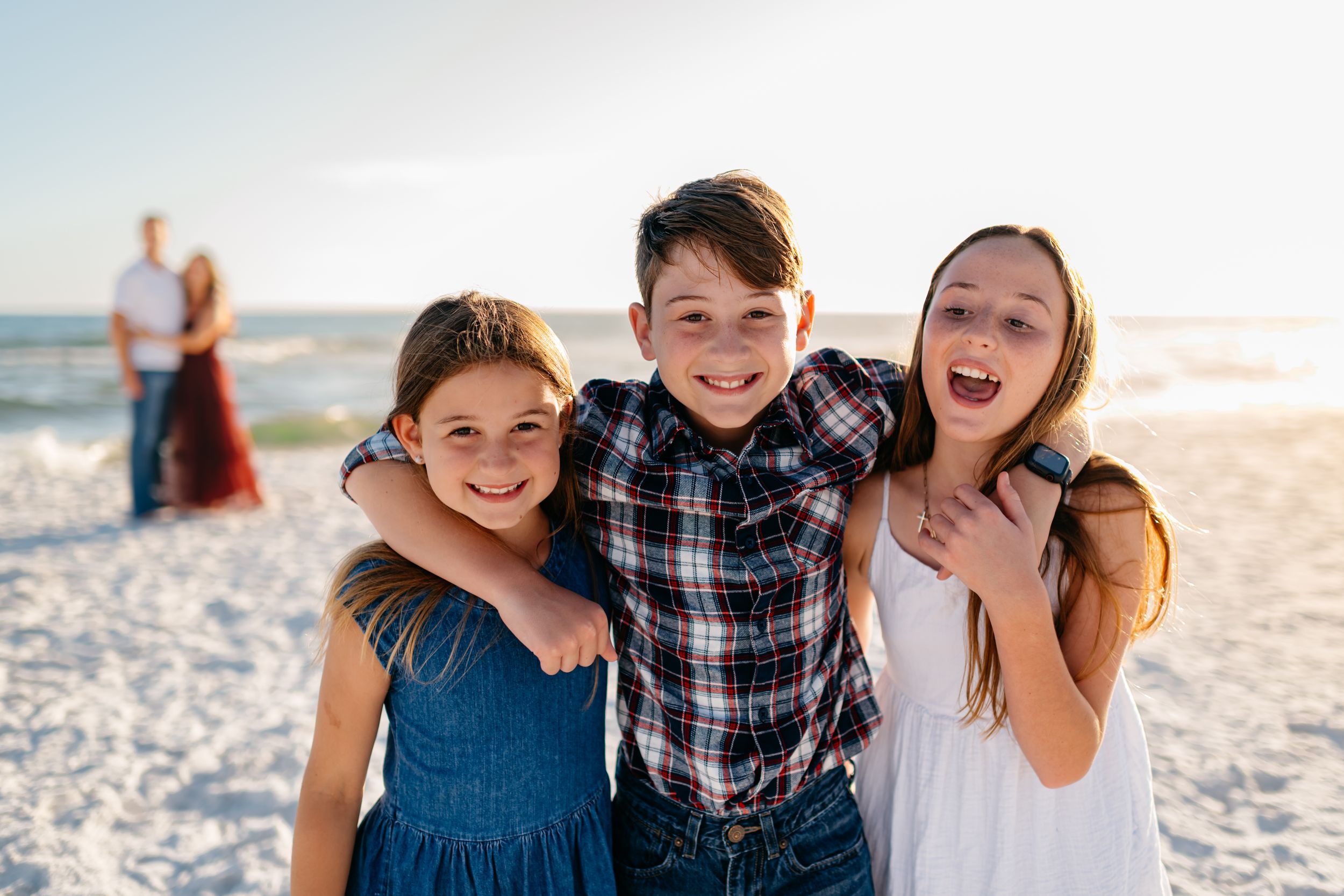 Family enjoying a sunny day at the beach with joyful expressions and casual attire.