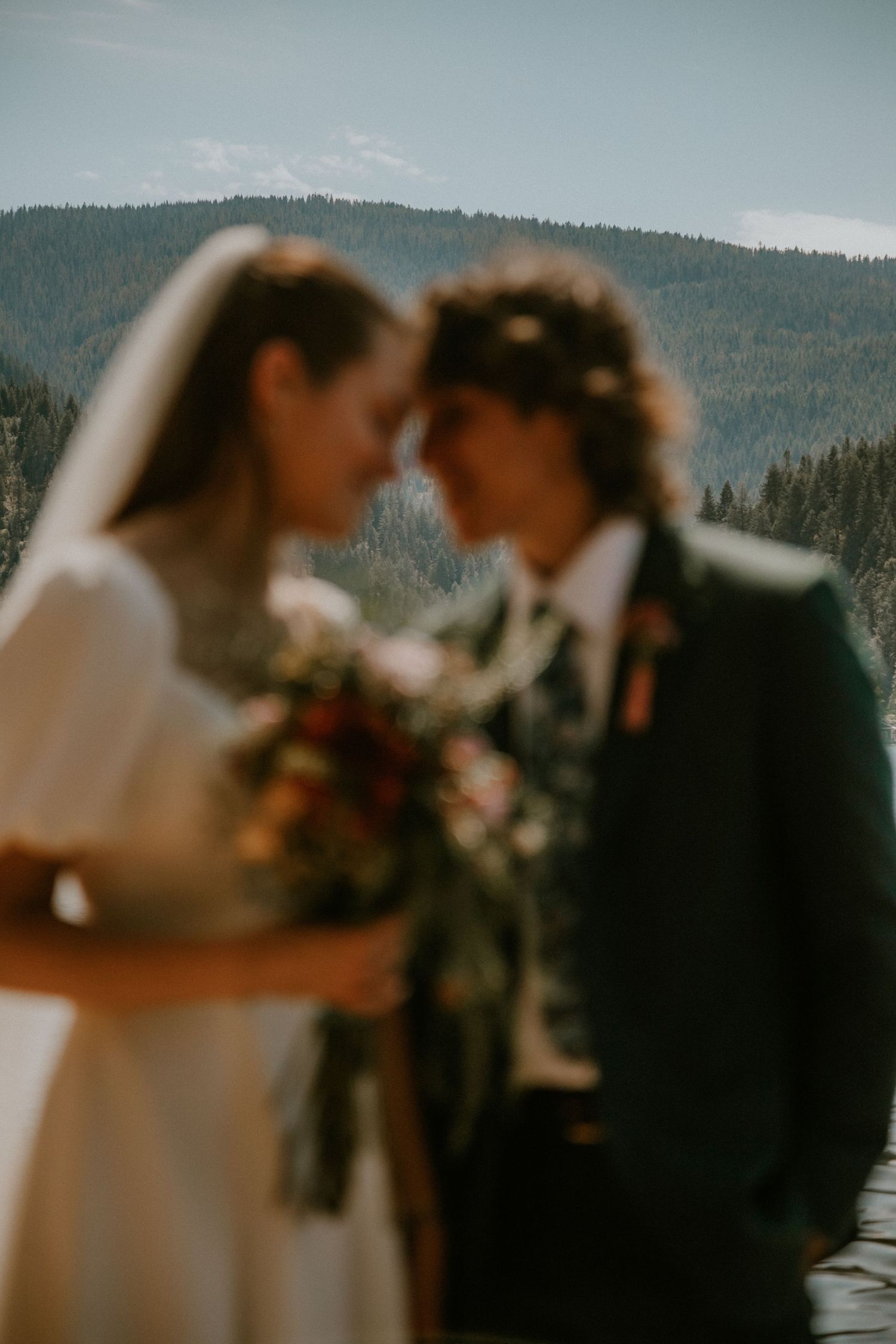 A romantic wedding couple shares an intimate moment against a backdrop of mountain forests on their special day.