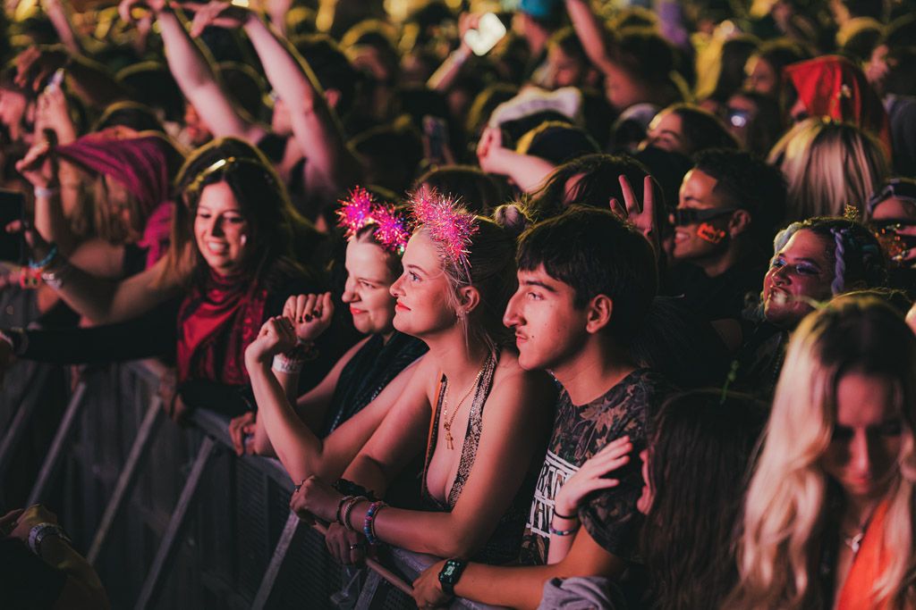 Concert crowd enjoying live music performance with colorful pink lighting at a nighttime event.