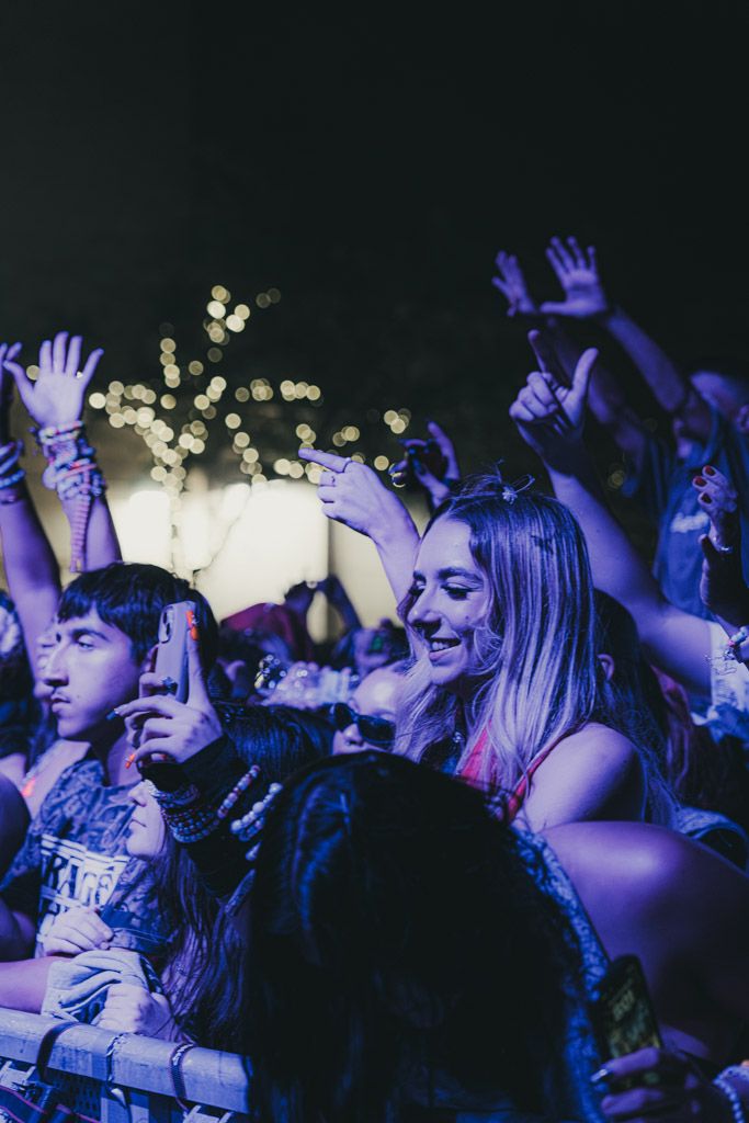 Concert crowd illuminated by blue lights raises their hands in excitement during a live music performance.