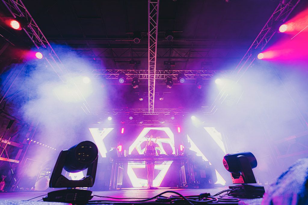 Stage lighting equipment and fog machines create a dramatic atmosphere with blue and pink hues at a concert venue.