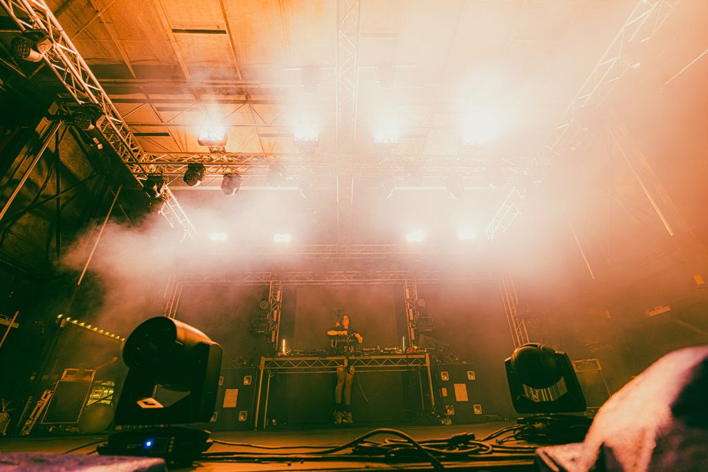 Concert stage illuminated in orange and red lights with smoke effects creating a dramatic atmosphere during performance.