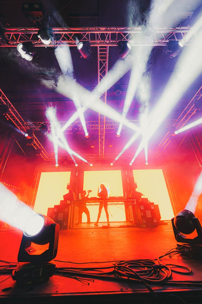 Concert stage lighting setup with dramatic white spotlights and red illumination creating an atmospheric performance environment.