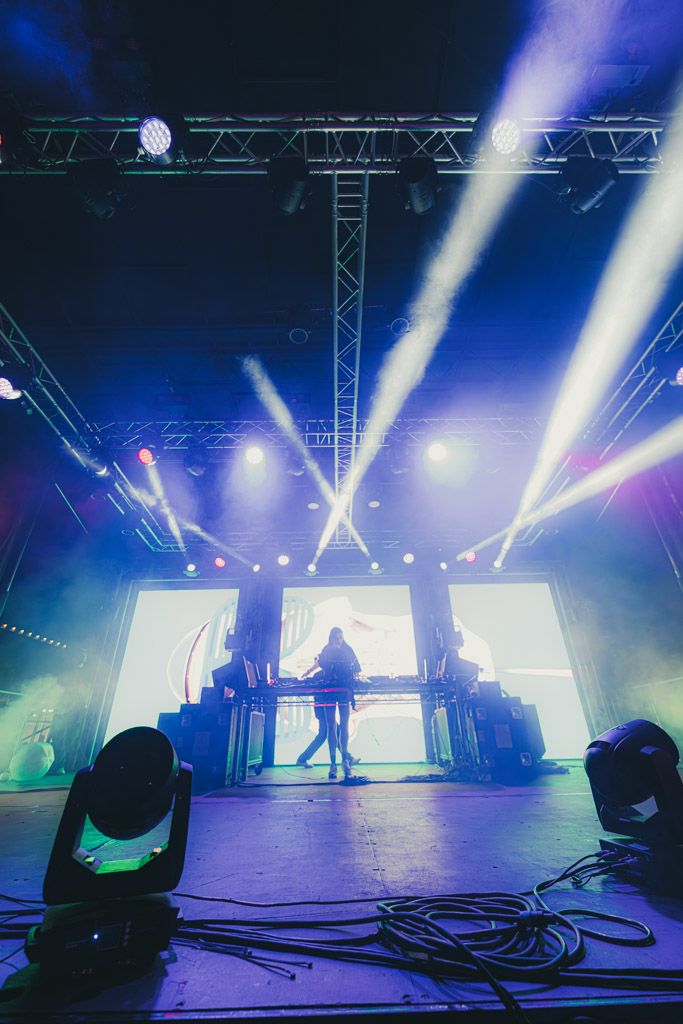 Concert stage with dramatic blue and white spotlights illuminating a performer silhouetted against bright LED screens.