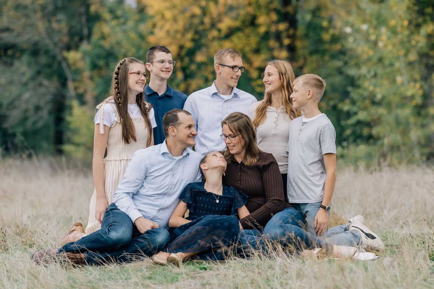 Happy family of seven sitting and posing together in a sunlit autumn meadow.