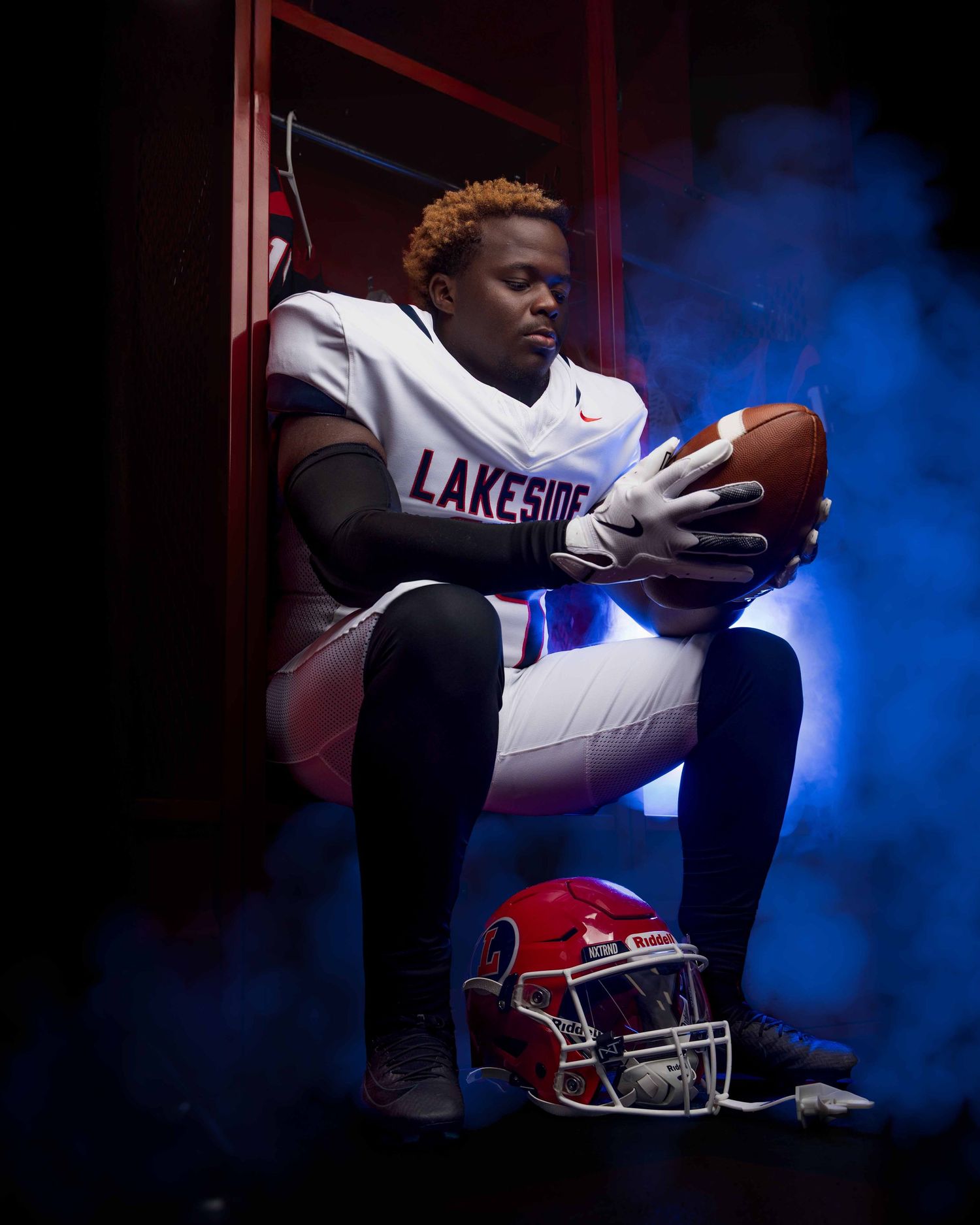 A football player sits in dramatic lighting with red and blue illumination creating a moody sports portrait.