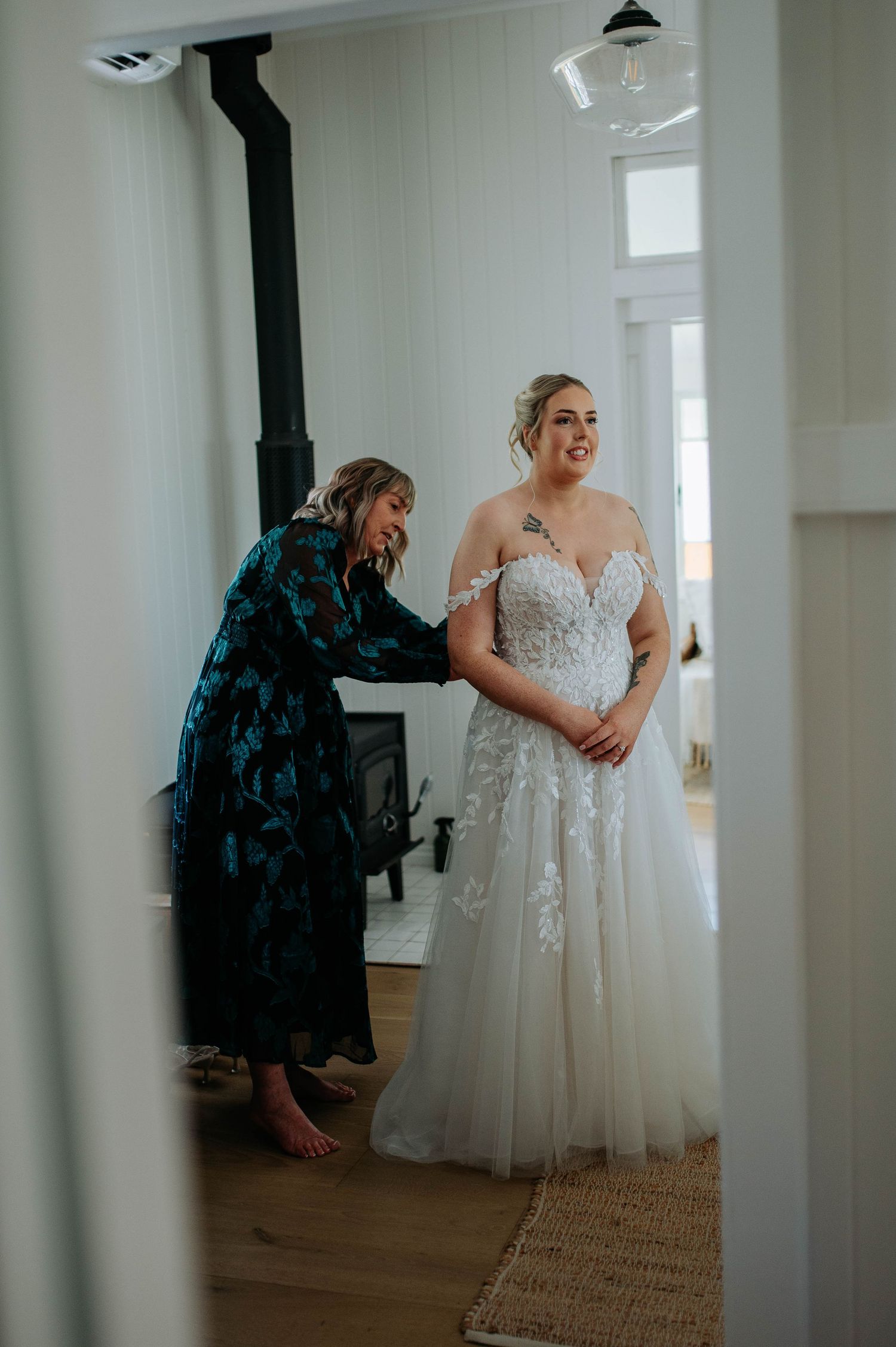A wedding dress fitting moment captured in a bright room with hardwood floors and white walls.