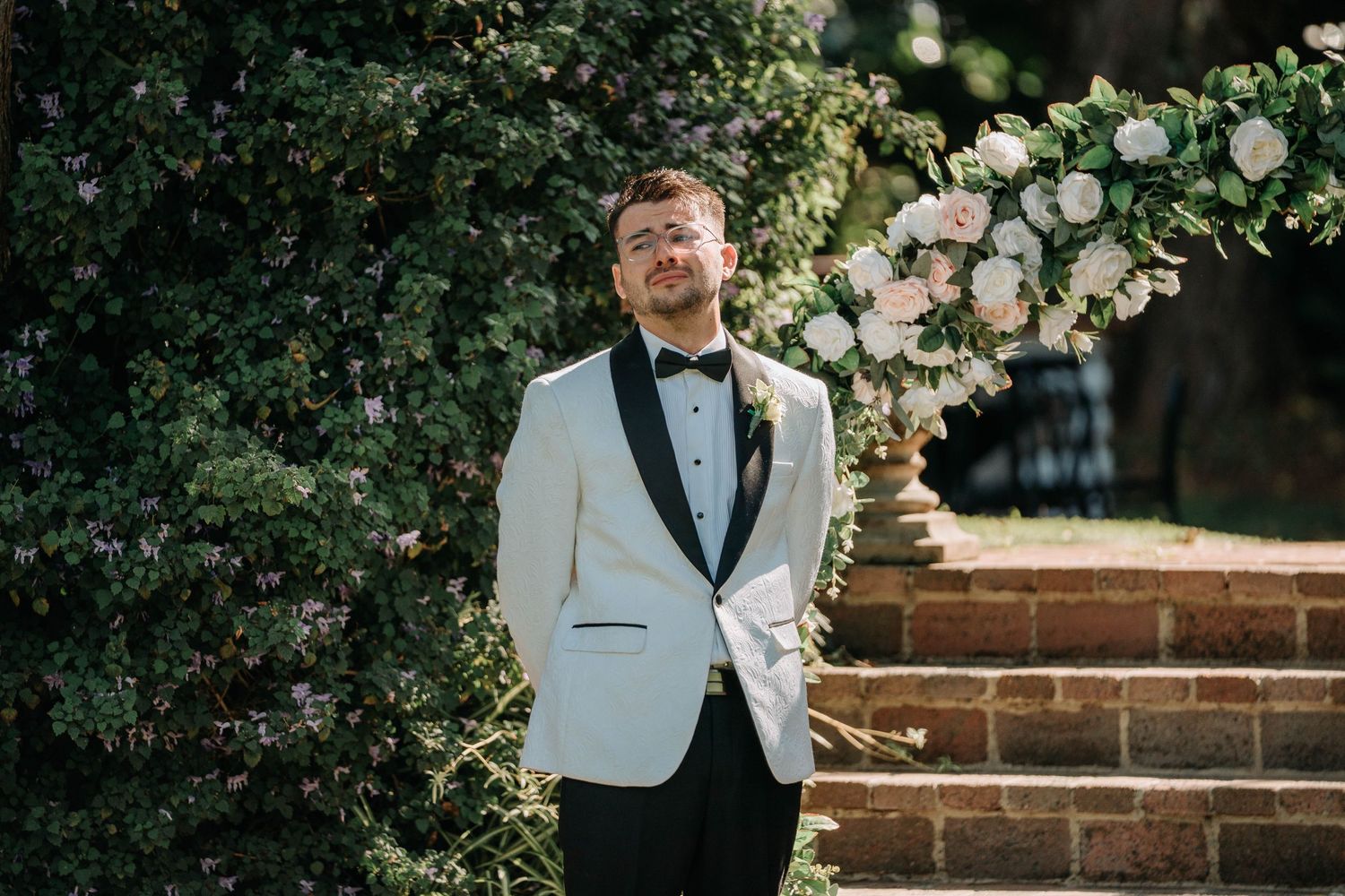 A wedding couple embraces under a floral arch during an outdoor garden ceremony.