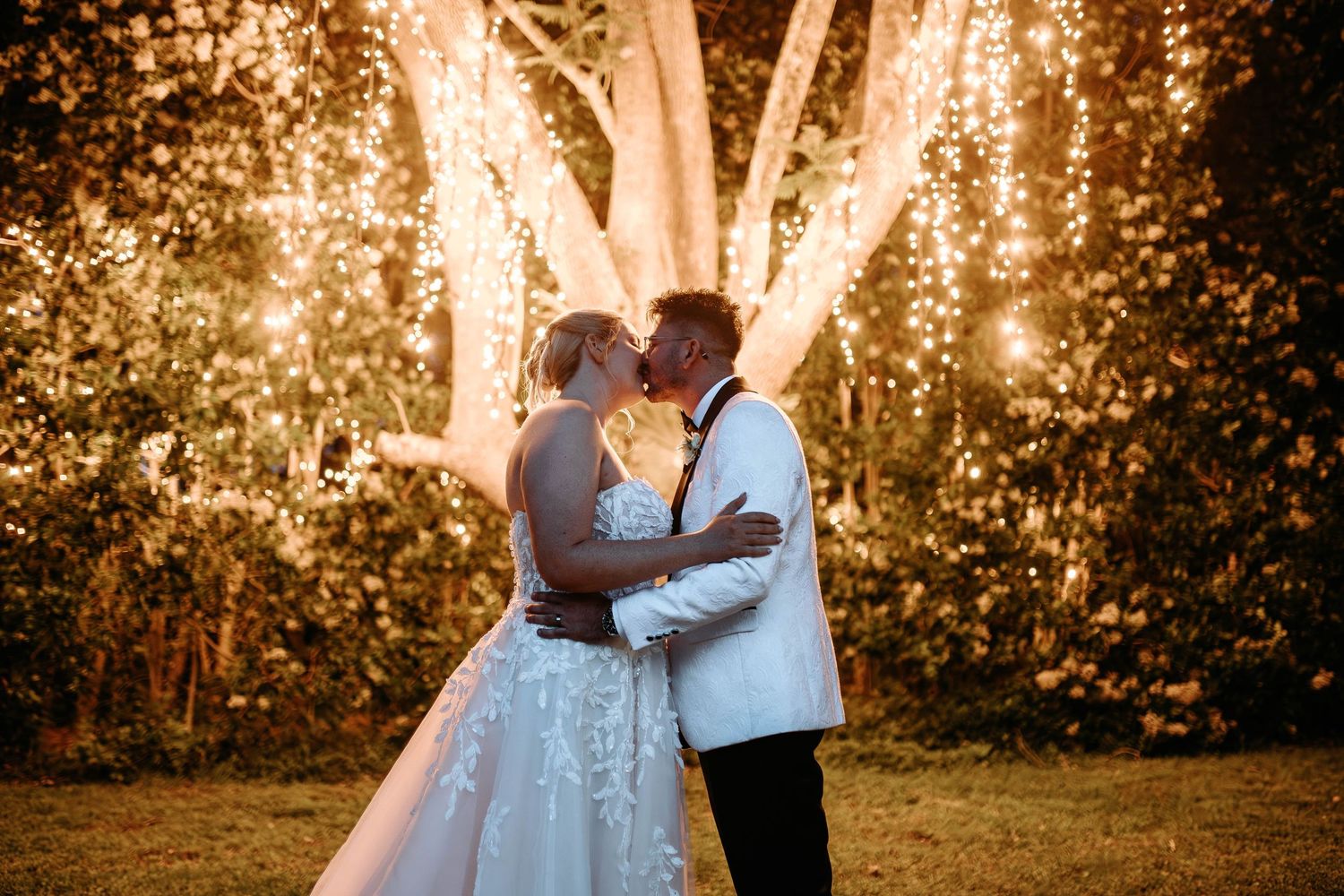A couple embraces during golden hour in front of glowing trees creating a romantic backlit silhouette effect.