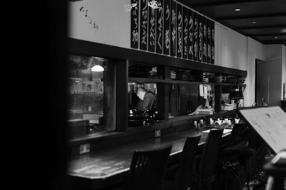 Dark interior bar setting with backlit glass shelves displaying bottles and glassware in moody ambient lighting.