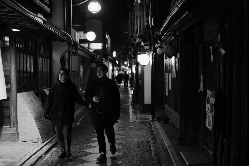 People walking down a narrow alley at night in Kyoto's traditional Pontocho district illuminated by lanterns.